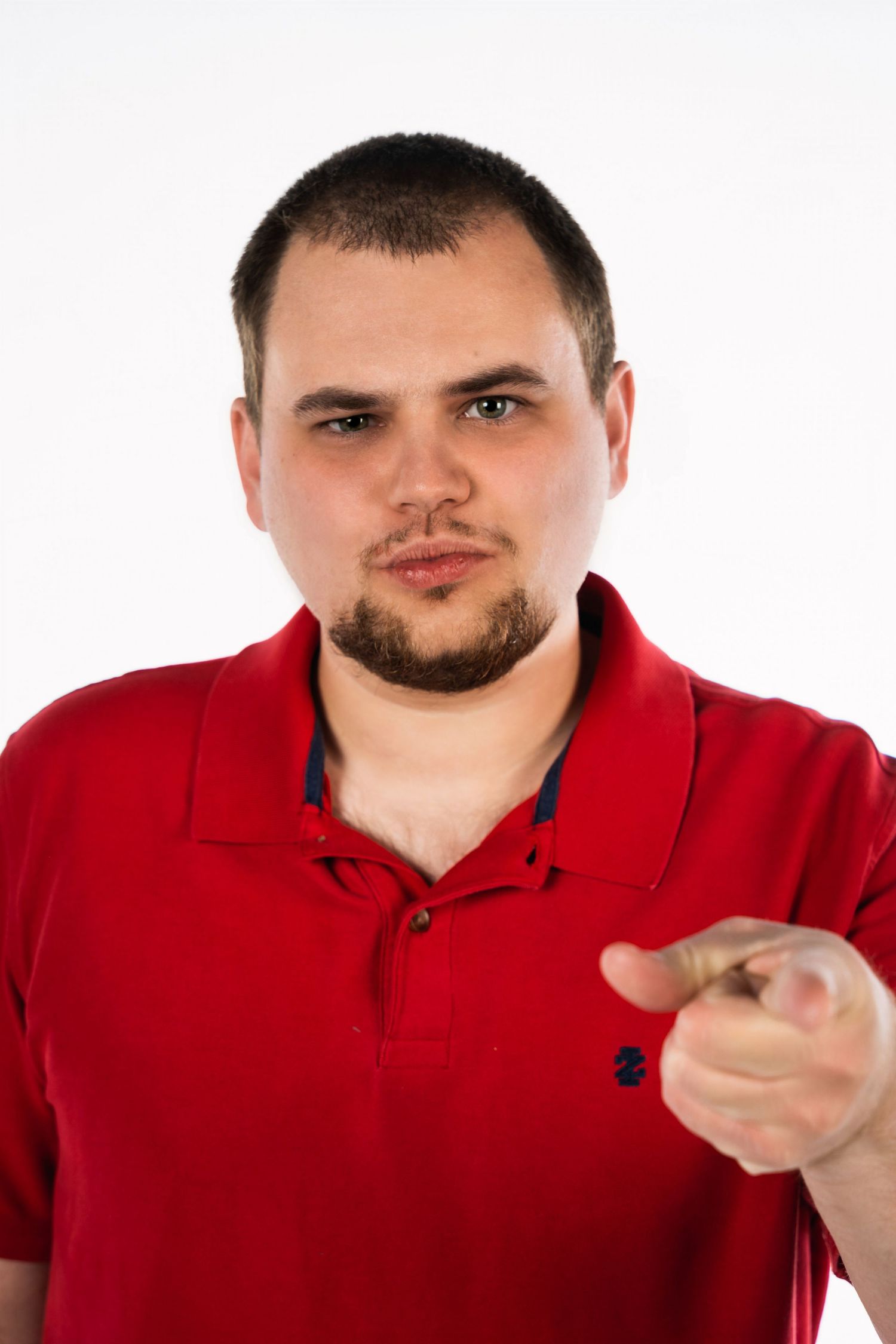 Man in red polo shirt points at camera against white background.
