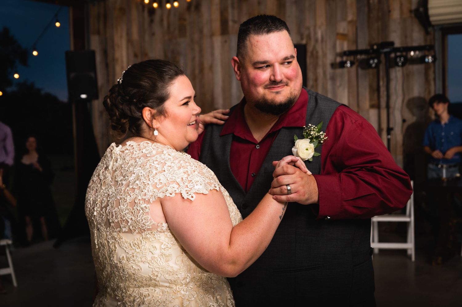 A couple shares a dance together in a rustic barn venue with wooden walls and ambient lighting.