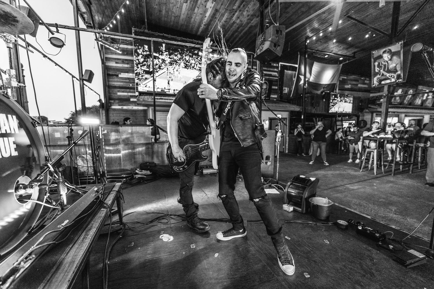 Black and white photo of musicians performing on a small stage in a bar setting.