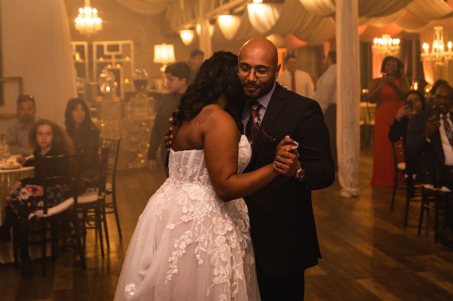 A couple shares an intimate dance during their wedding reception in a warmly lit ballroom.