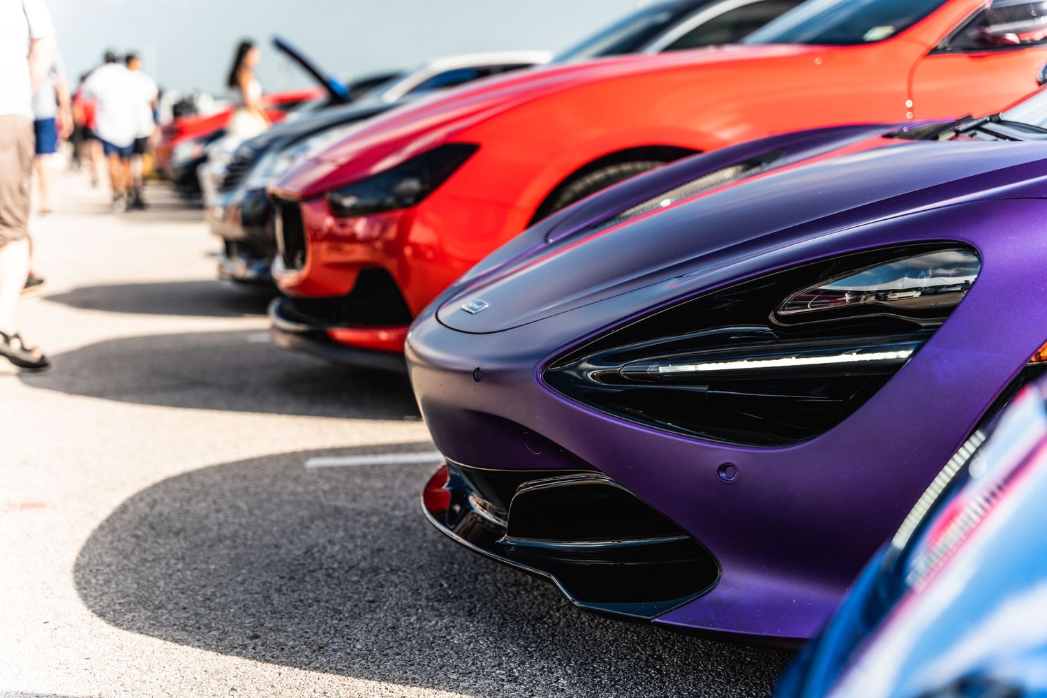 Row of colorful McLaren supercars including purple and red models showcasing their front bumper designs.