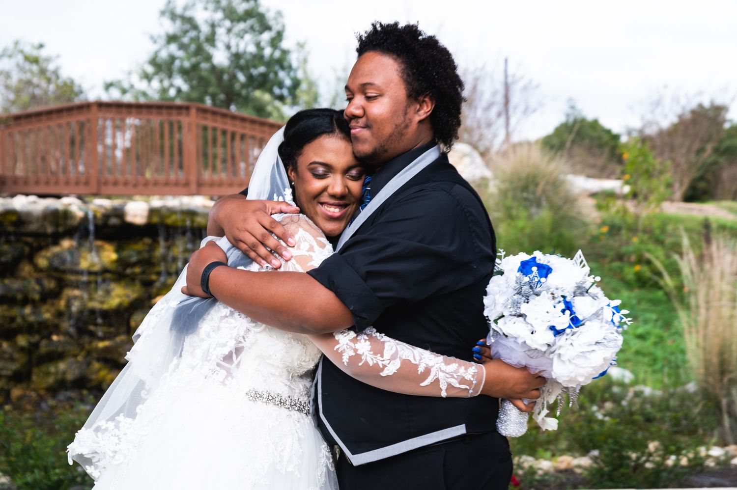 Newlyweds share an intimate moment outdoors while holding blue and white bouquet.