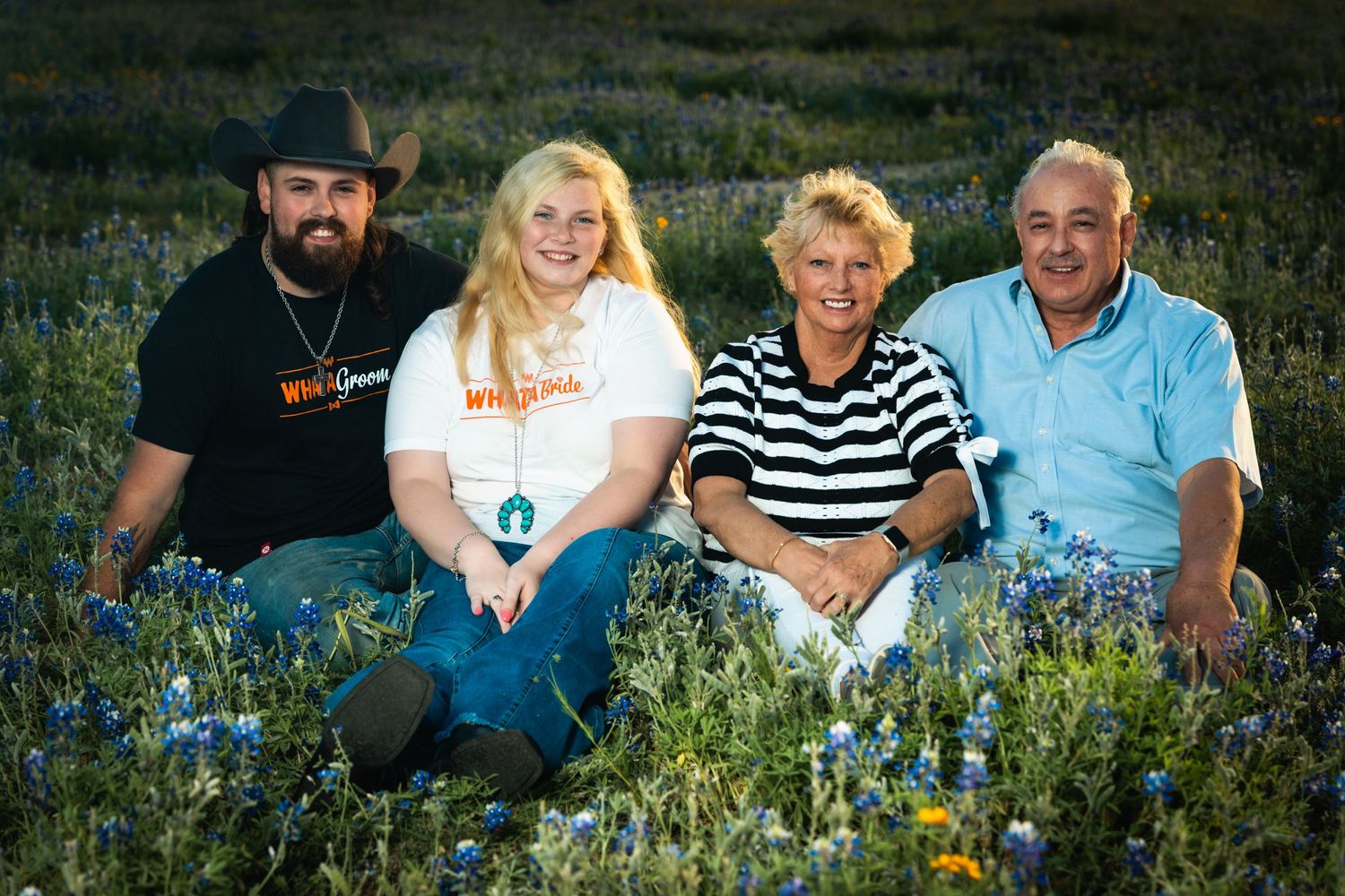 A group of four people sitting together in a field of blue wildflowers.