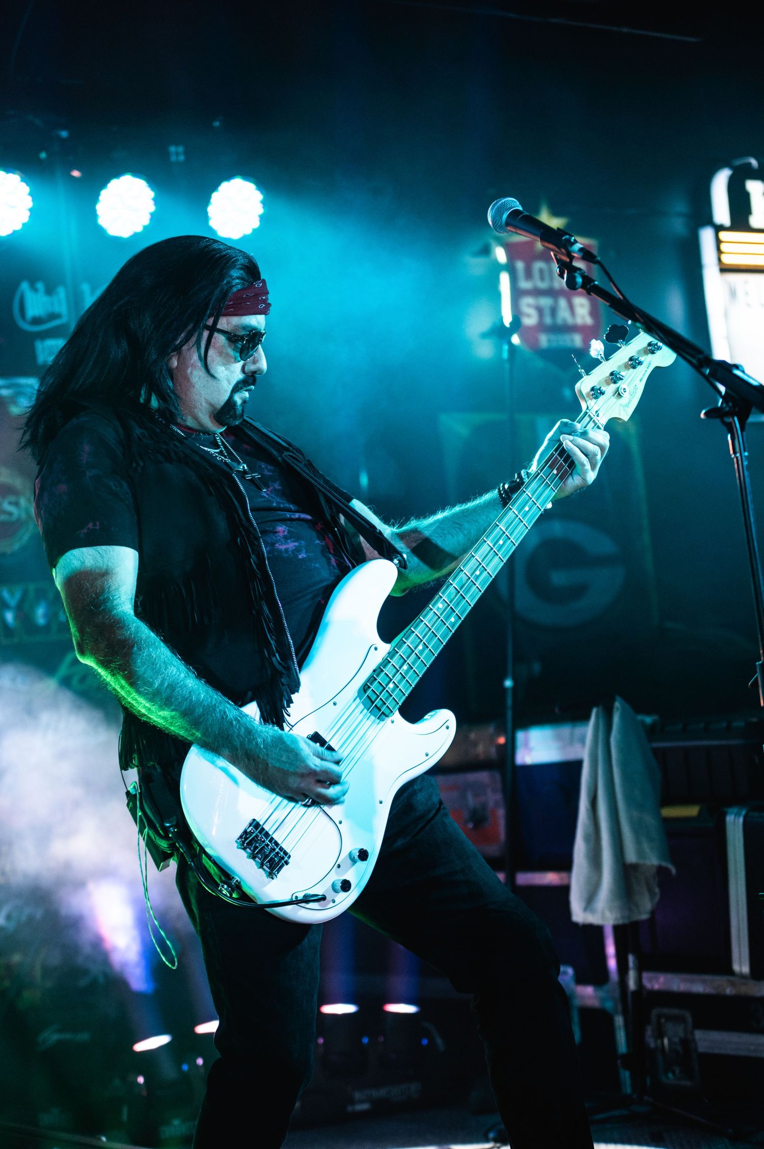 Bass guitarist performs on stage with blue lighting and fog effects.