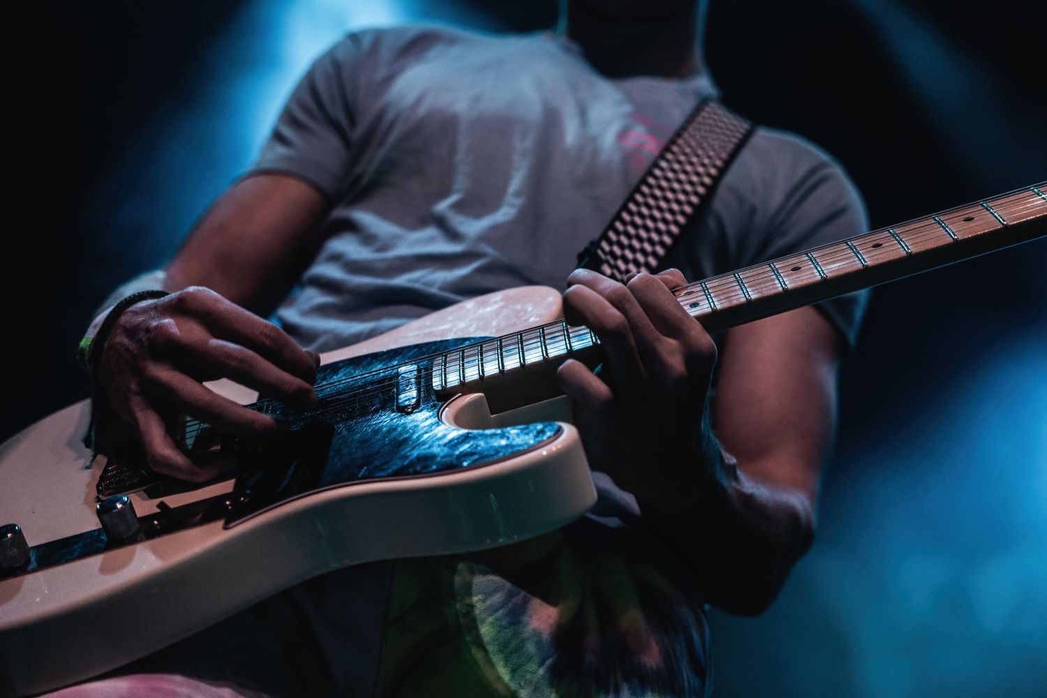 Close-up of musician playing electric guitar under blue spotlight on dark stage.