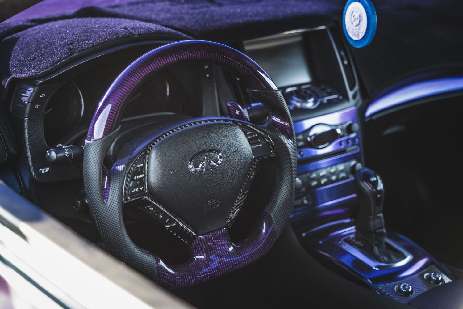 Modern Infiniti interior with purple accents and leather-wrapped steering wheel.