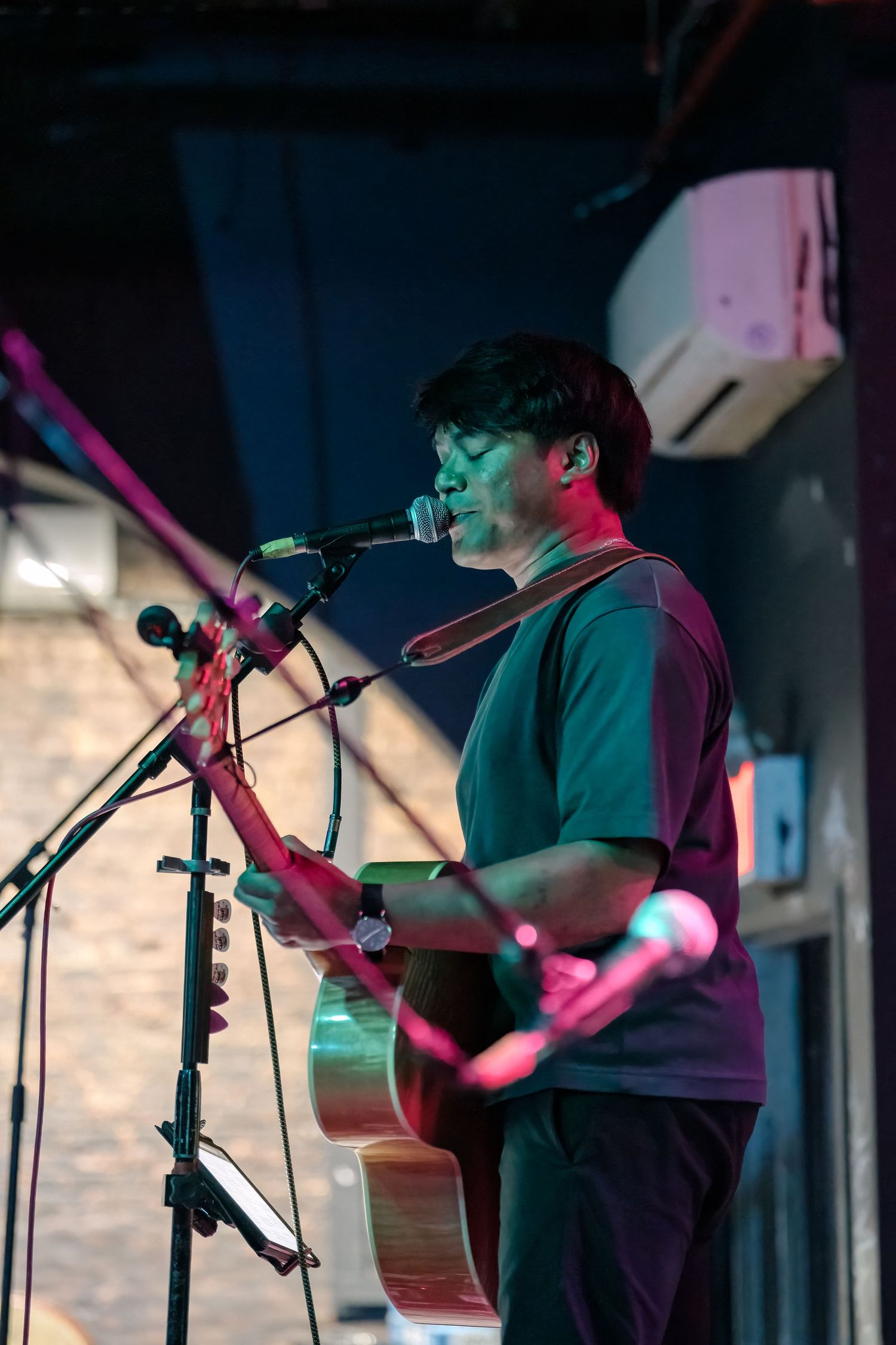 Performer plays acoustic guitar on stage illuminated by vibrant blue and pink lighting effects.