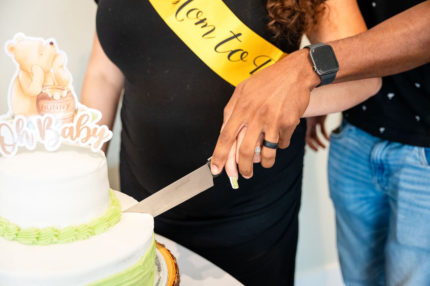 Hands shown cutting into a white and green decorated baby shower cake.