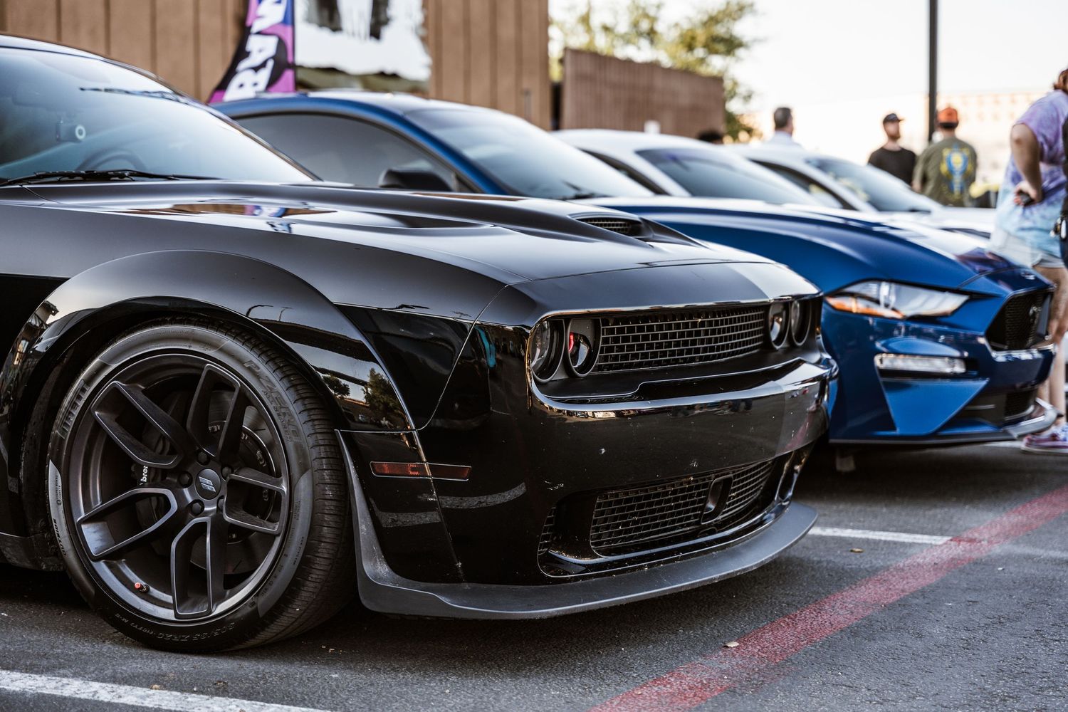 Black Dodge Challenger with custom wheels parked at car show.
