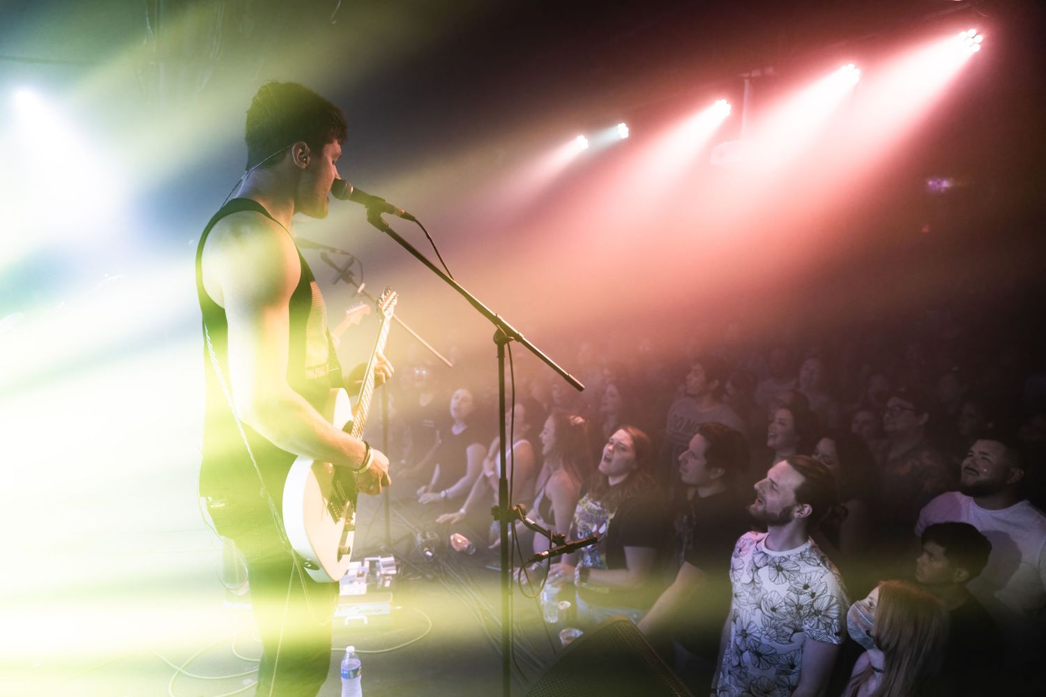Performer silhouetted against pink stage lights while singing to crowd at concert venue.