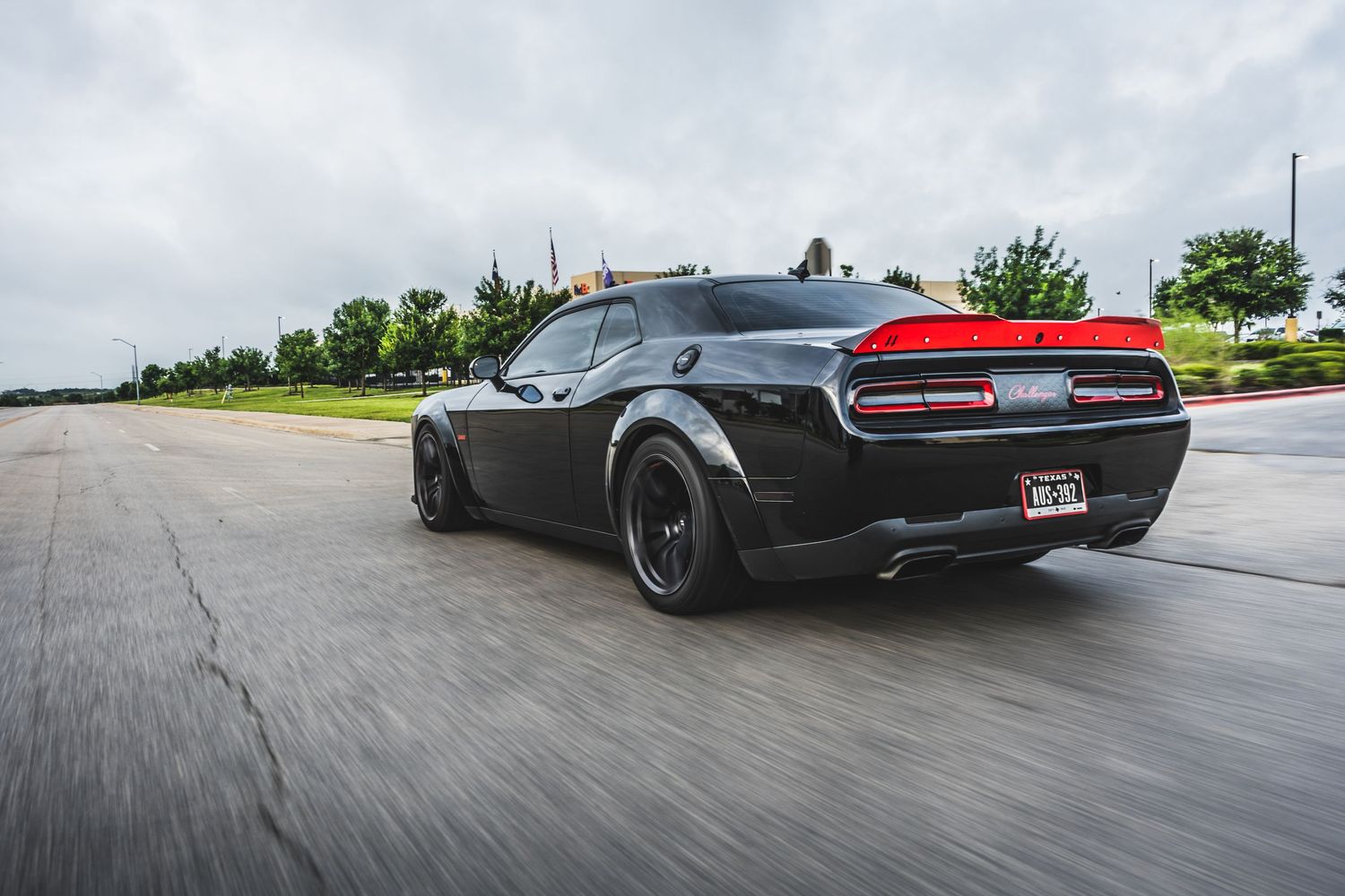 Black Dodge Challenger with dark wheels speeding down a wet road.