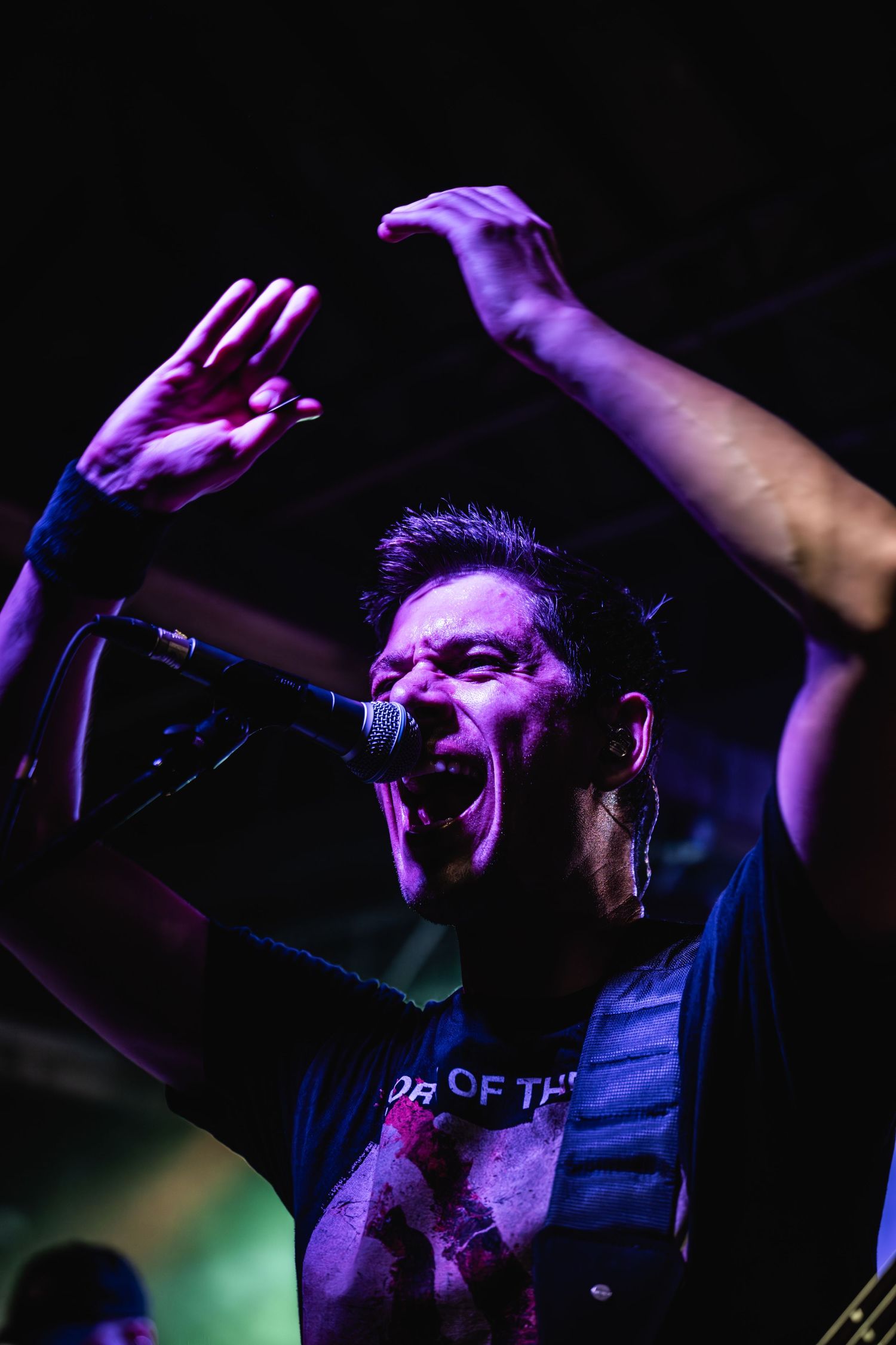 Passionate vocalist performs with arms raised under dramatic purple stage lighting.