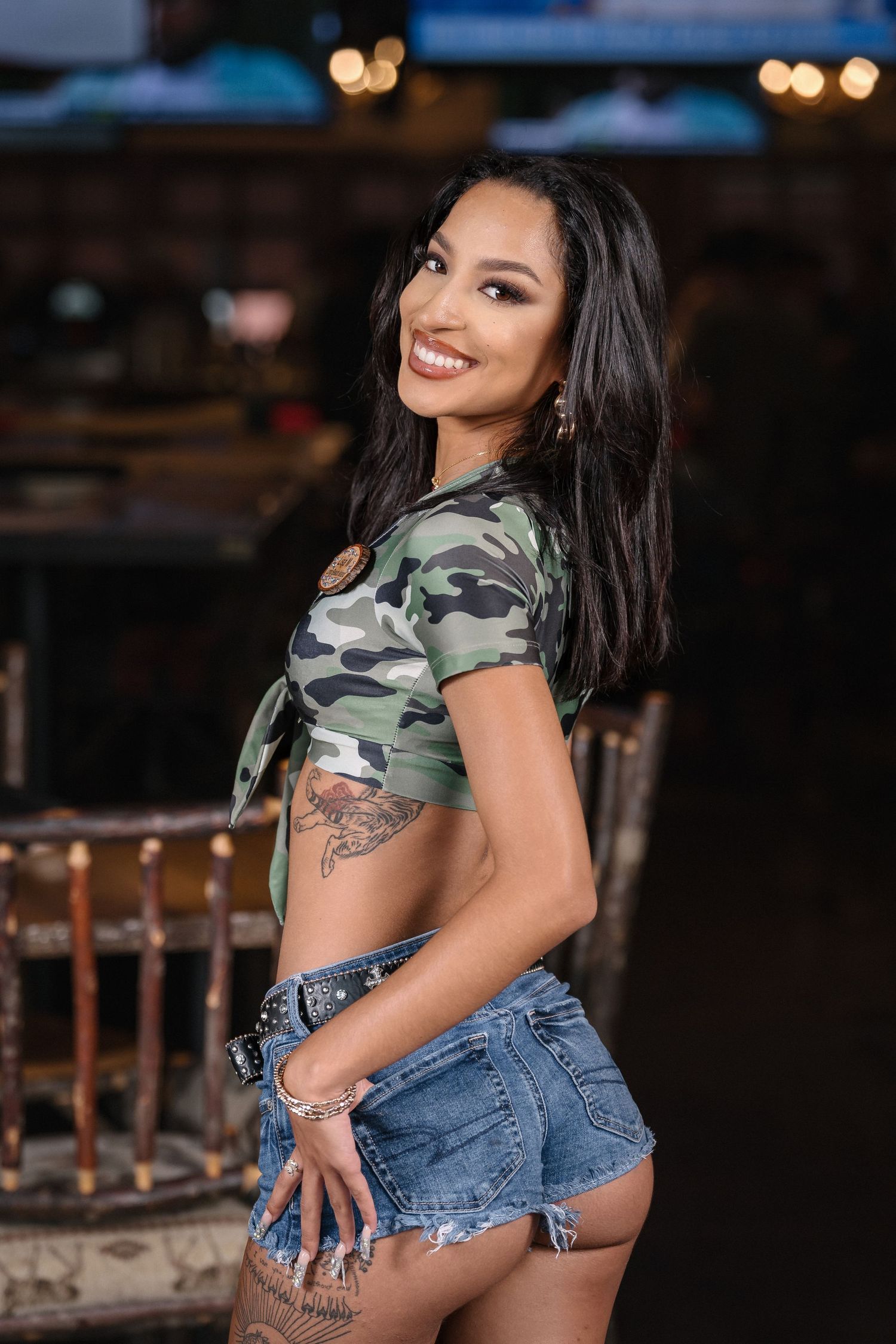 Promotional photo of camouflage crop top and denim shorts in bar setting.