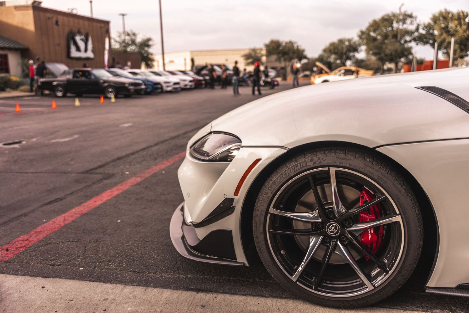 White sports car with custom wheels and red brake calipers at a car meet.