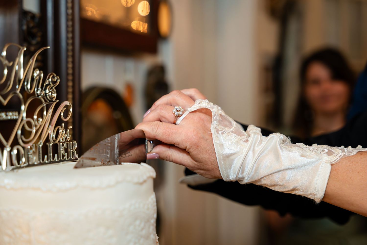 Close-up of hands cutting into an elegant white wedding cake at a reception.