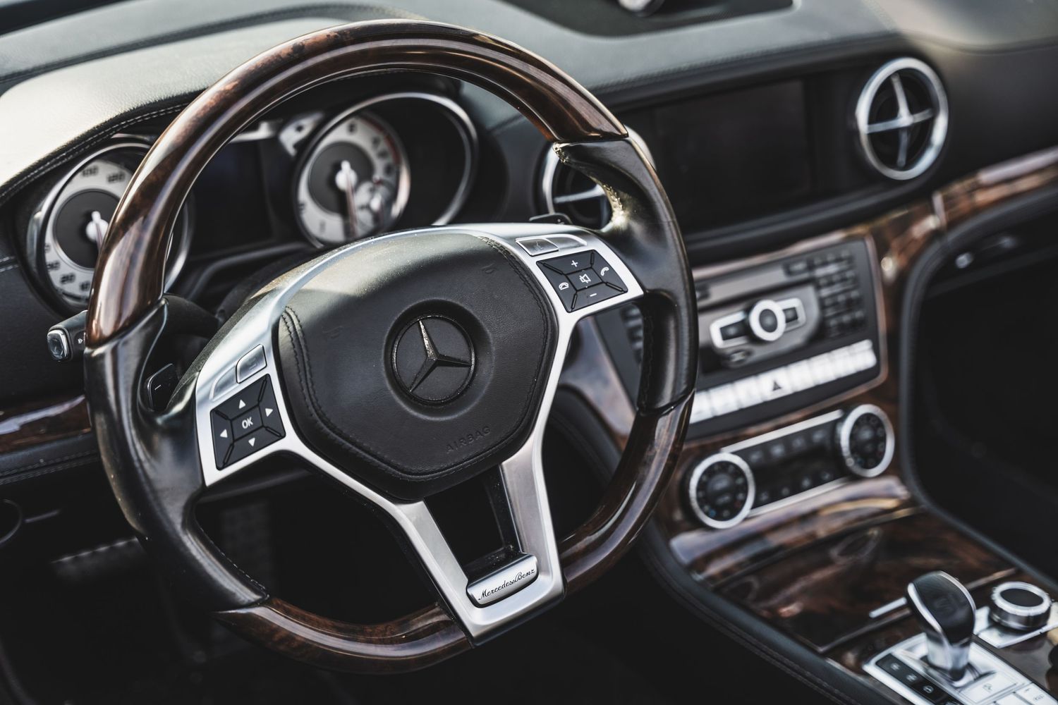 Interior view of Mercedes-Benz steering wheel and dashboard with wood trim.