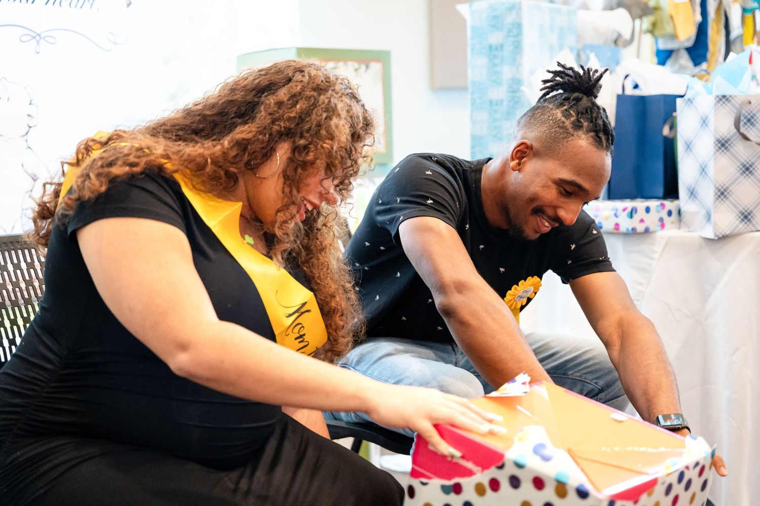 Two people opening gifts together at a festive baby shower celebration.