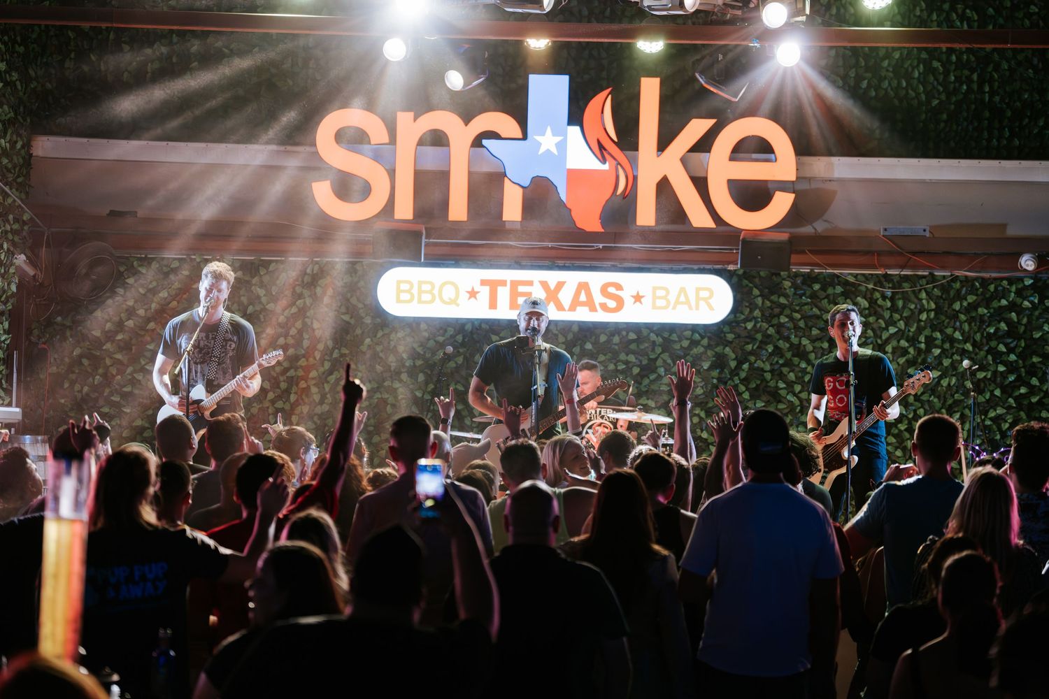Band performs on stage with dramatic lighting and Smoke BBQ Texas sign overhead.