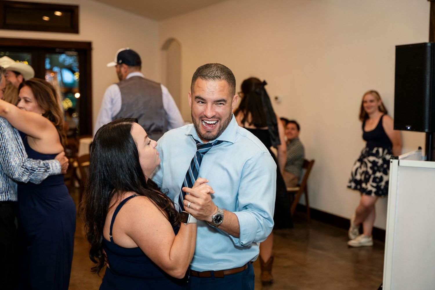 A couple shares a joyful moment dancing together at an indoor party with guests in the background.