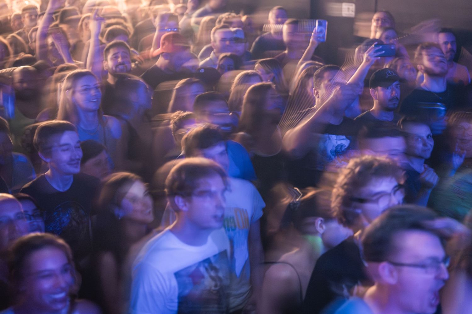 Blurred motion shot of enthusiastic concert audience with blue lighting effects.