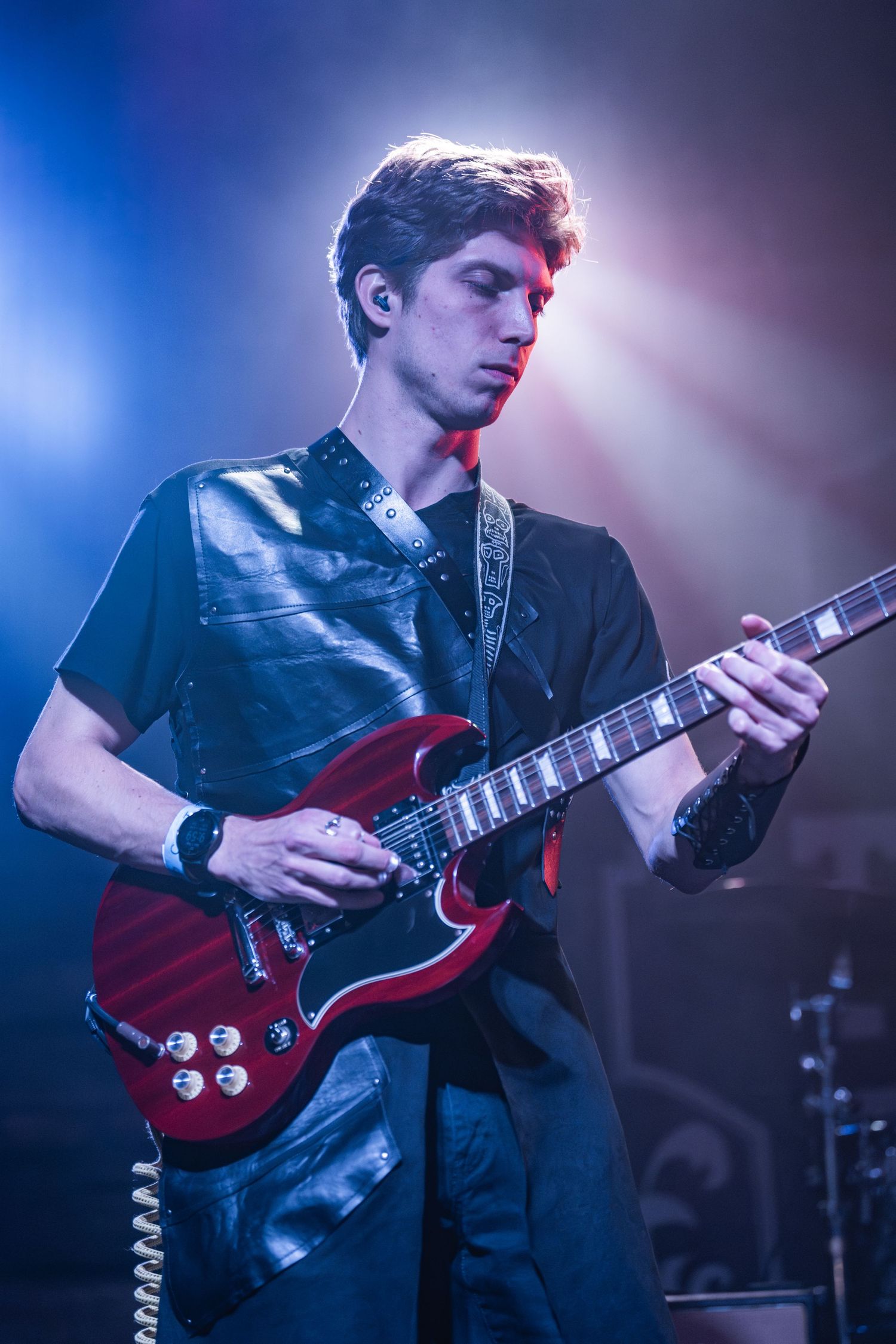 Musician playing red SG guitar under dramatic stage lighting during live performance.