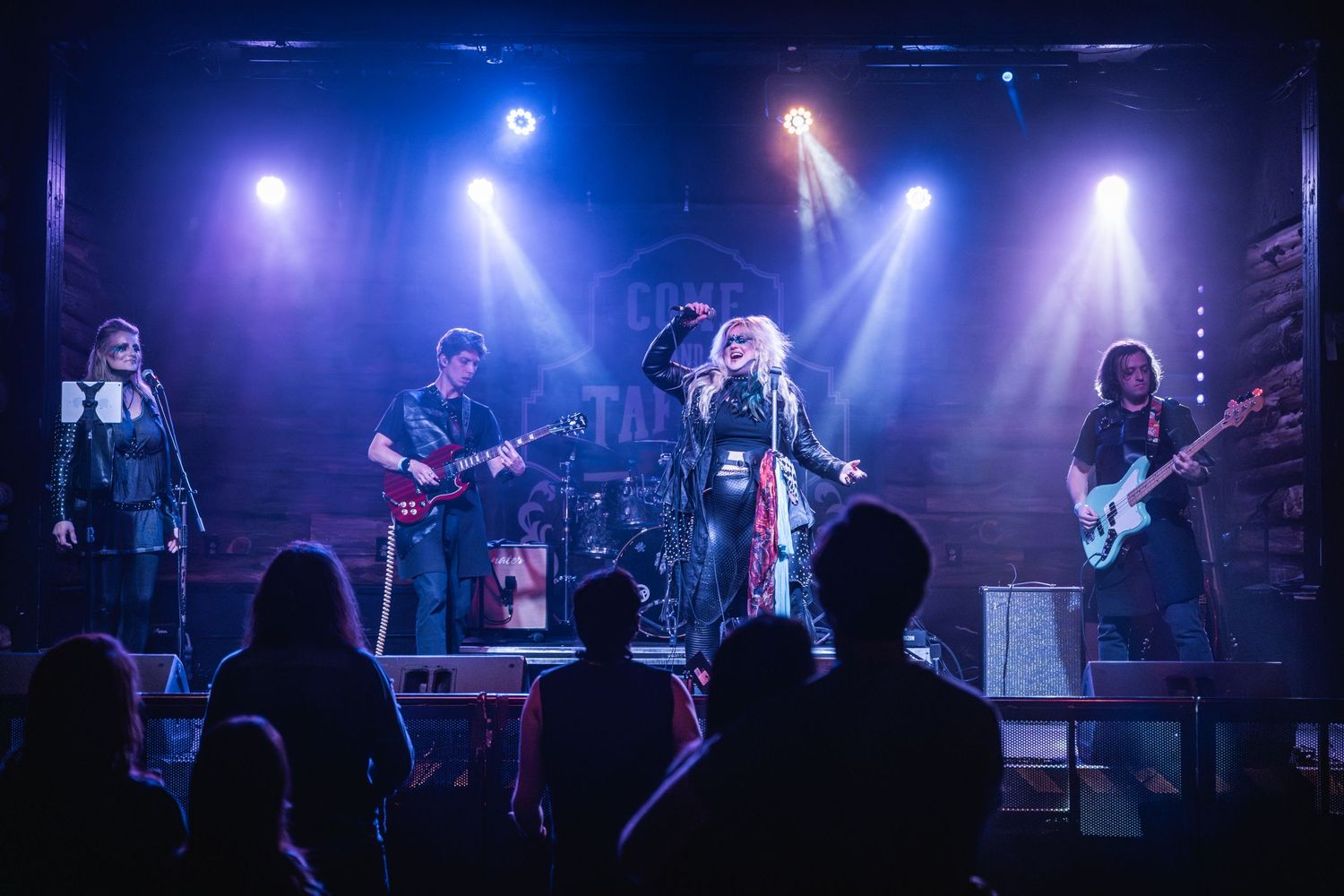 Band performs energetic live show with blue stage lights and crowd silhouettes below.