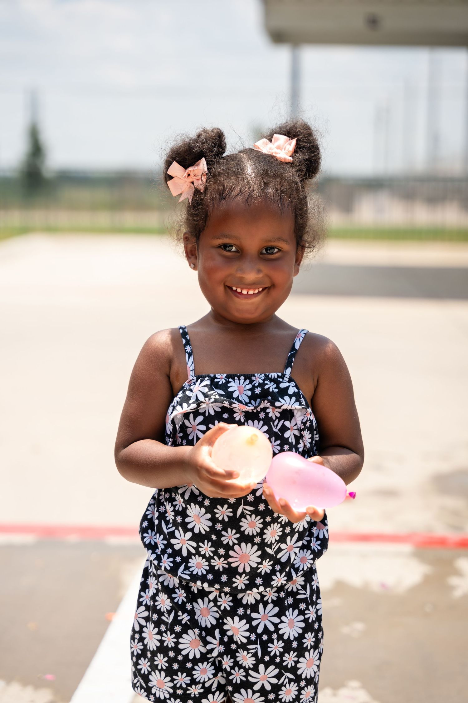 A young child in a floral dress holding something outdoors on a sunny day.