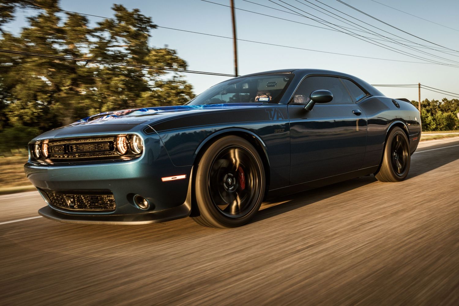 Dark metallic Dodge Challenger with black rims captured in dynamic rolling shot.