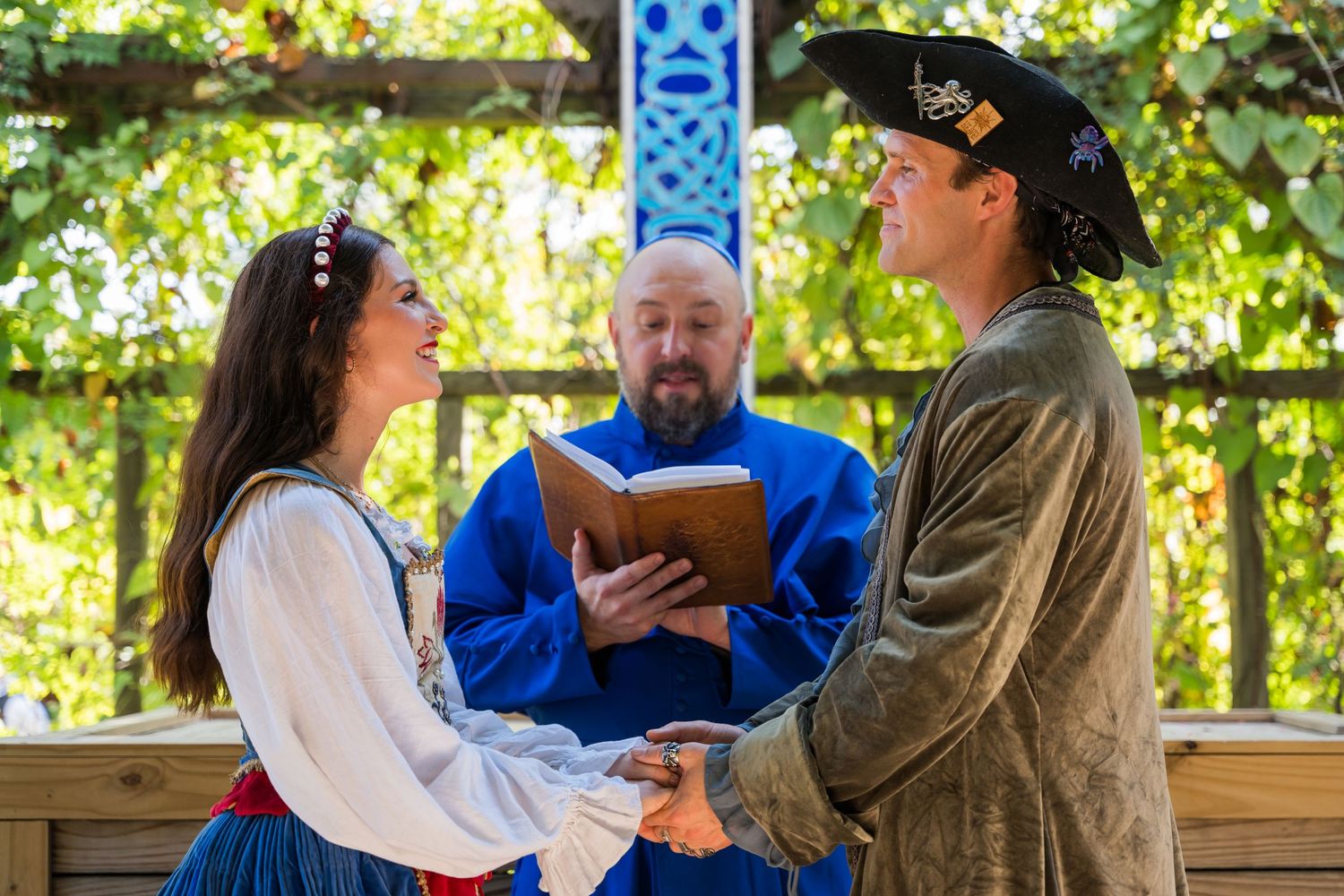 Renaissance fair wedding ceremony with minister in blue robe presiding over couple in period costumes.