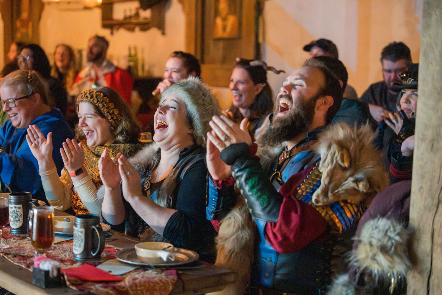 Enthusiastic audience members in medieval costumes cheering and clapping during a festival performance.