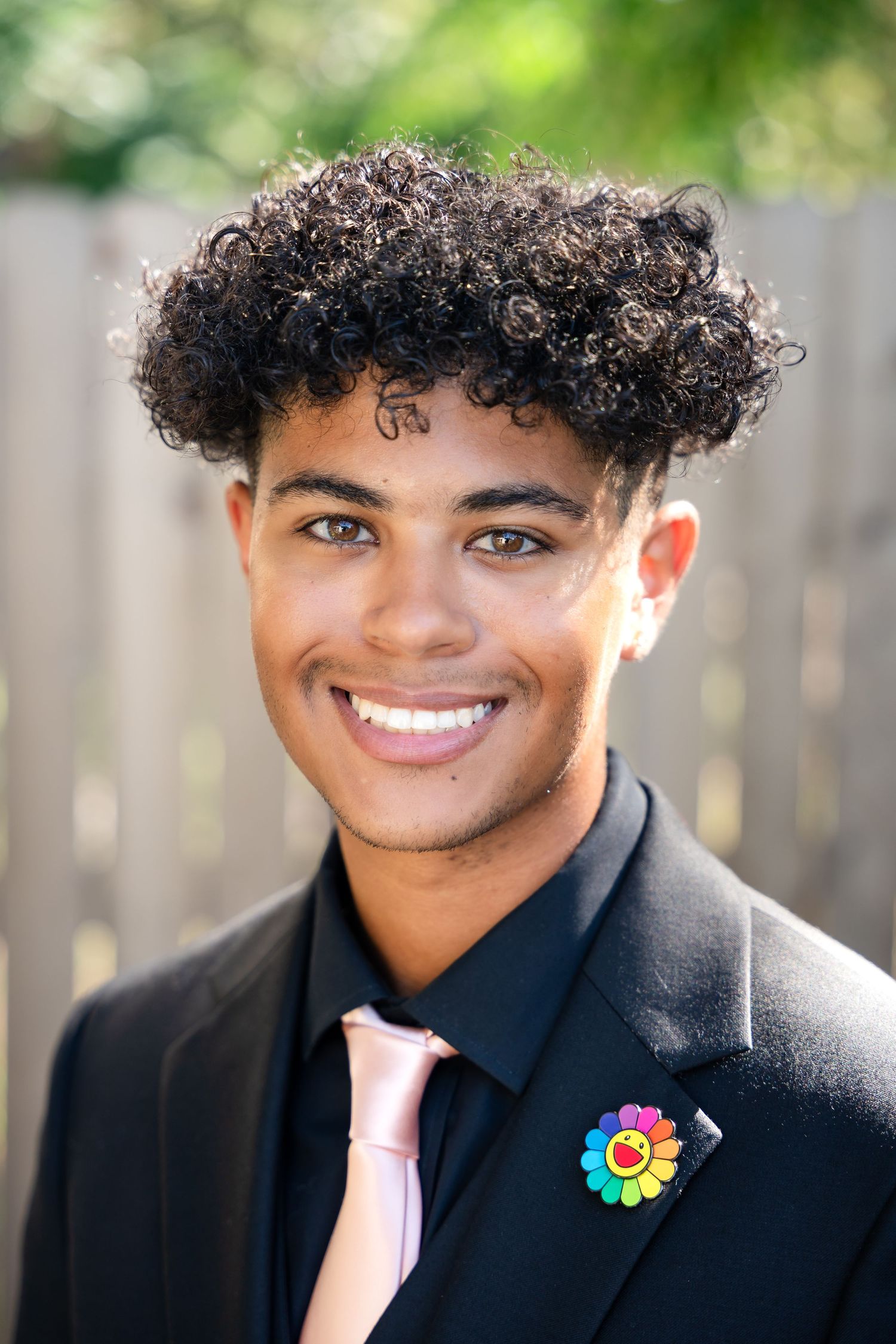Close-up portrait of someone wearing a black suit with pink tie and colorful floral pin.
