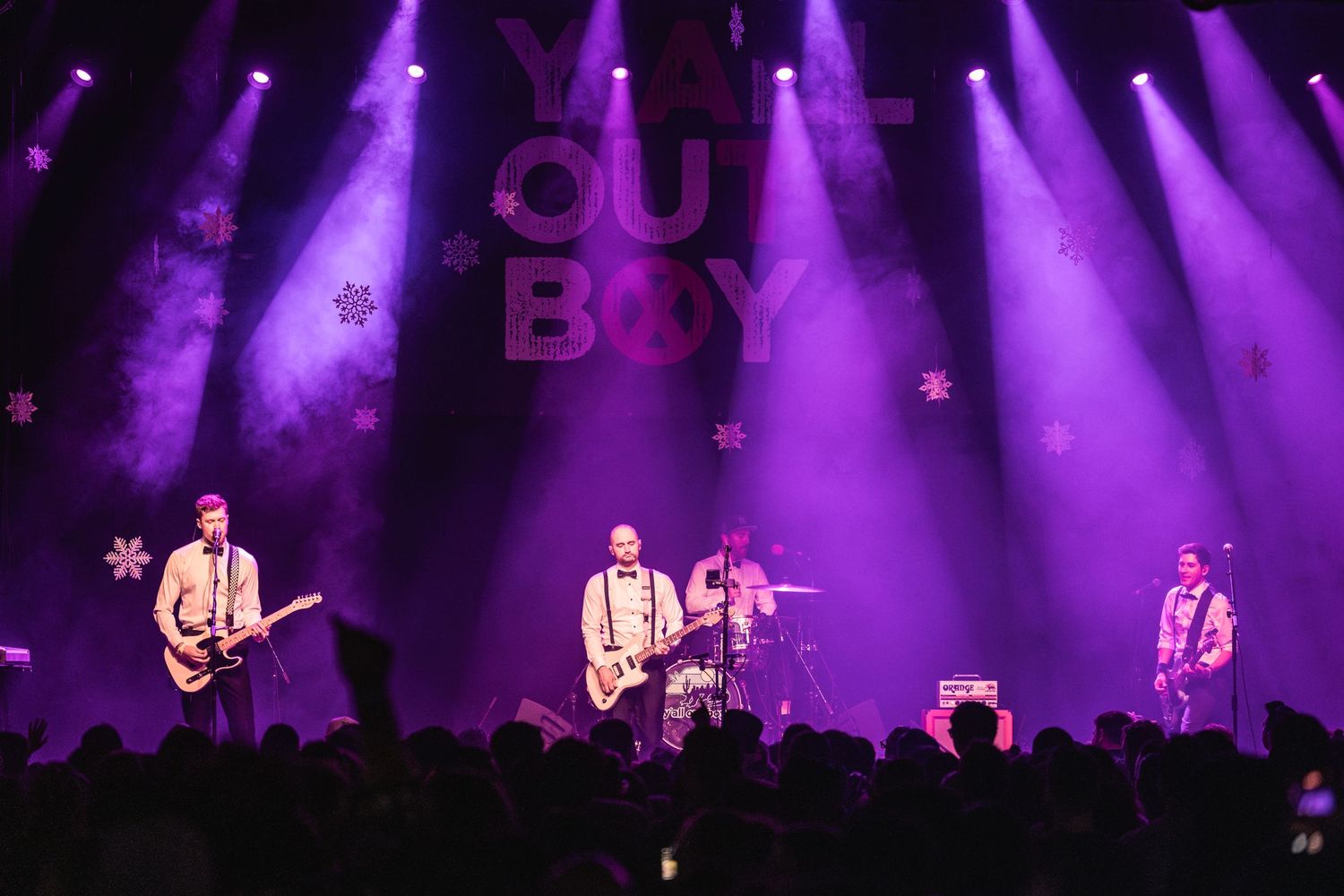 Rock band performs under purple stage lights with 'Our Boy' sign visible above.