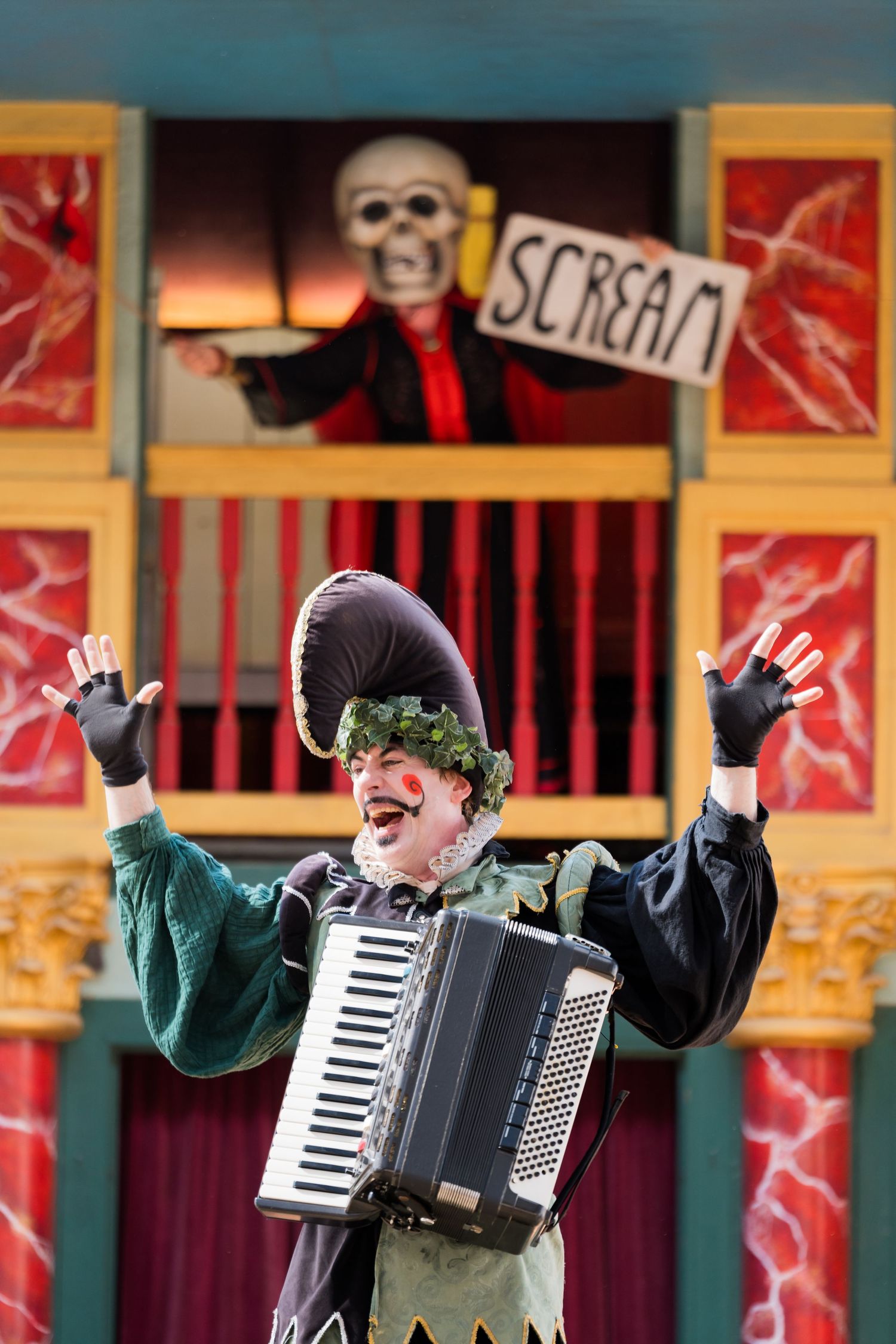 A costumed performer with an accordion gestures dramatically in front of a theatrical backdrop.