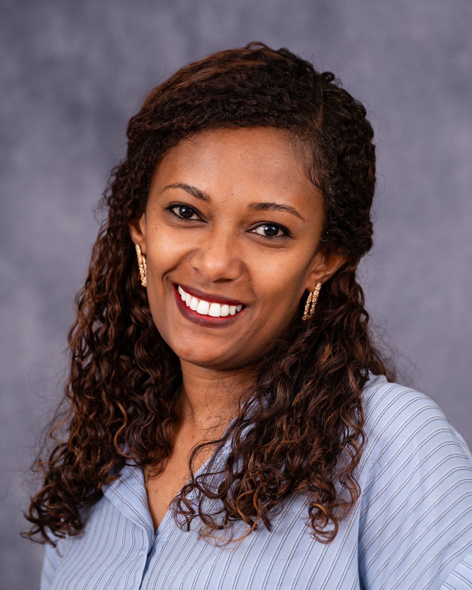 Professional portrait of woman with curly hair wearing business casual attire.