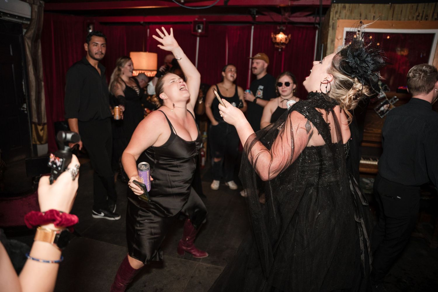 People dancing and celebrating at a party with red velvet curtains in the background.