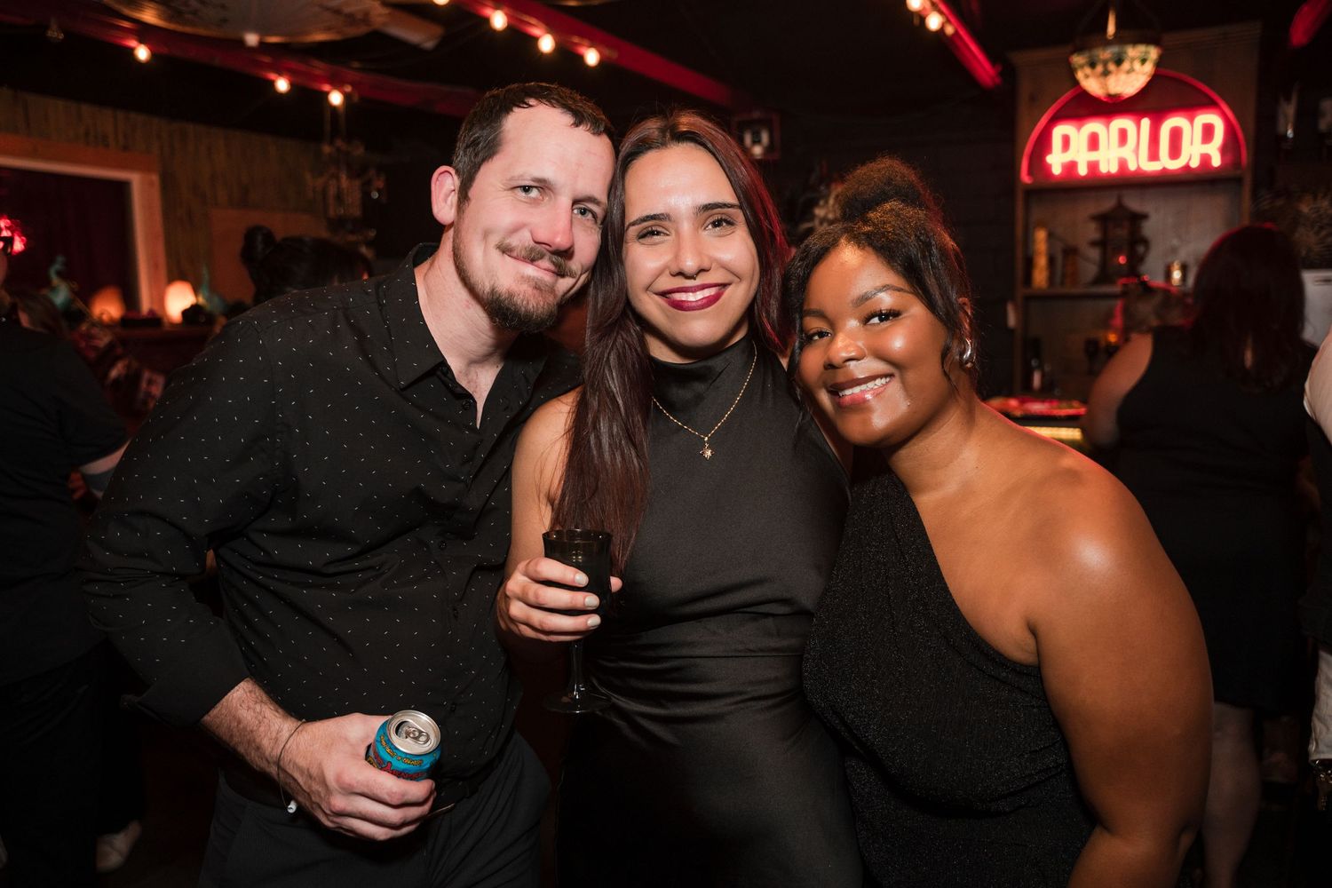 Party guests enjoying drinks and smiling at a dimly lit bar with neon signs.