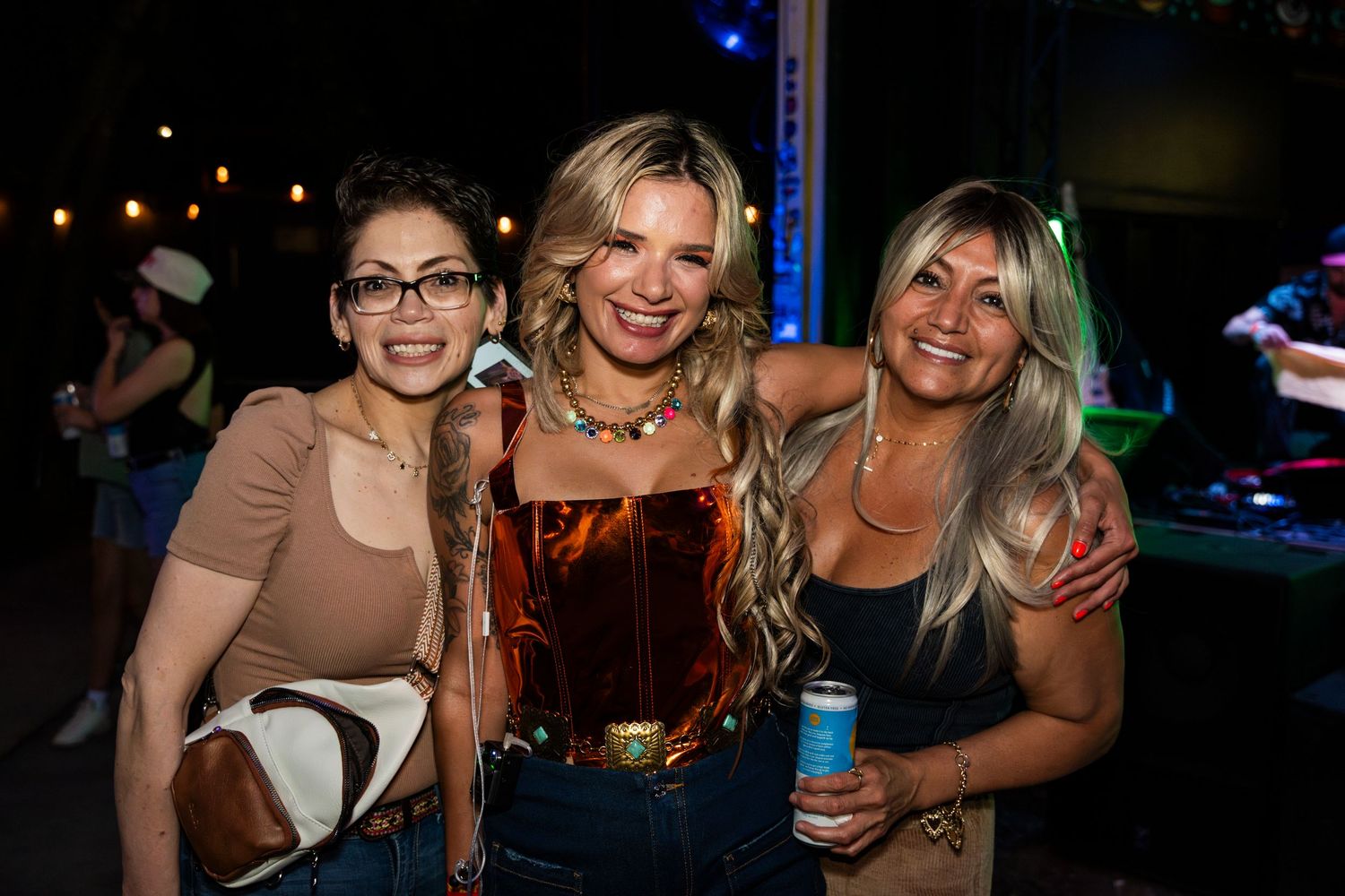Three friends pose together smiling at a nightclub with blue lighting in the background.