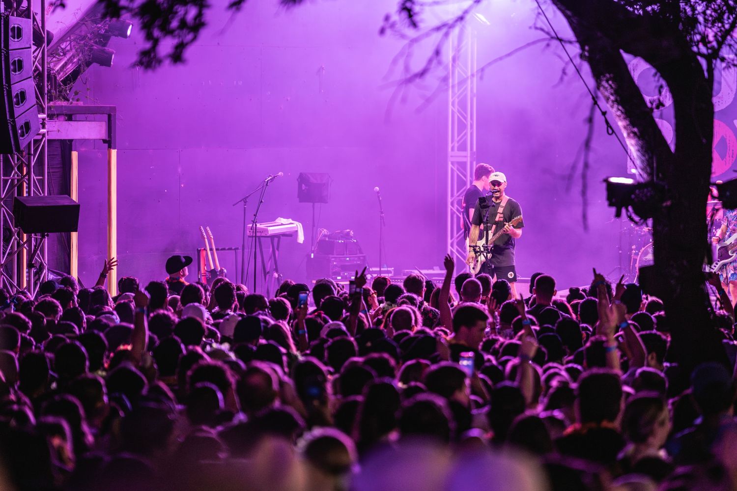 Concert crowd silhouetted against purple stage lighting during an outdoor nighttime performance.