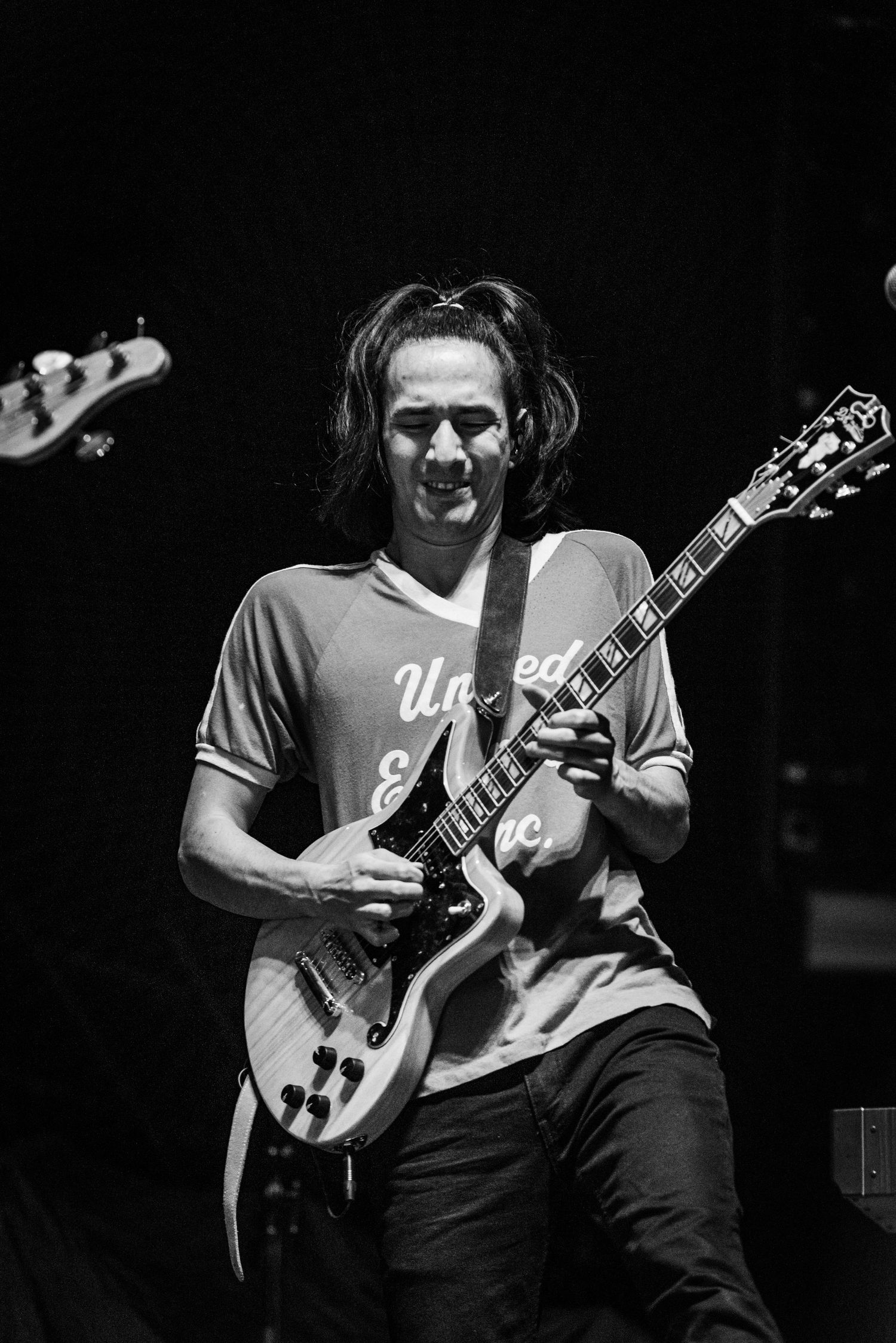 Black and white photo of guitarist playing on stage wearing casual t-shirt.