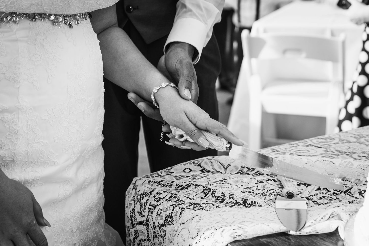 Close-up black and white shot of hands cutting into a wedding cake.