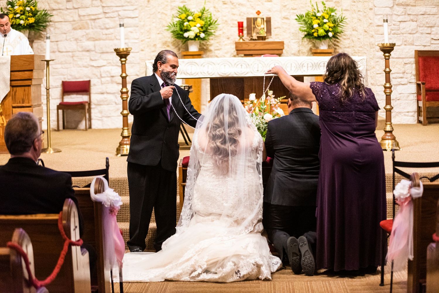 Wedding ceremony participants gather at the altar of a stone church with yellow floral decorations.