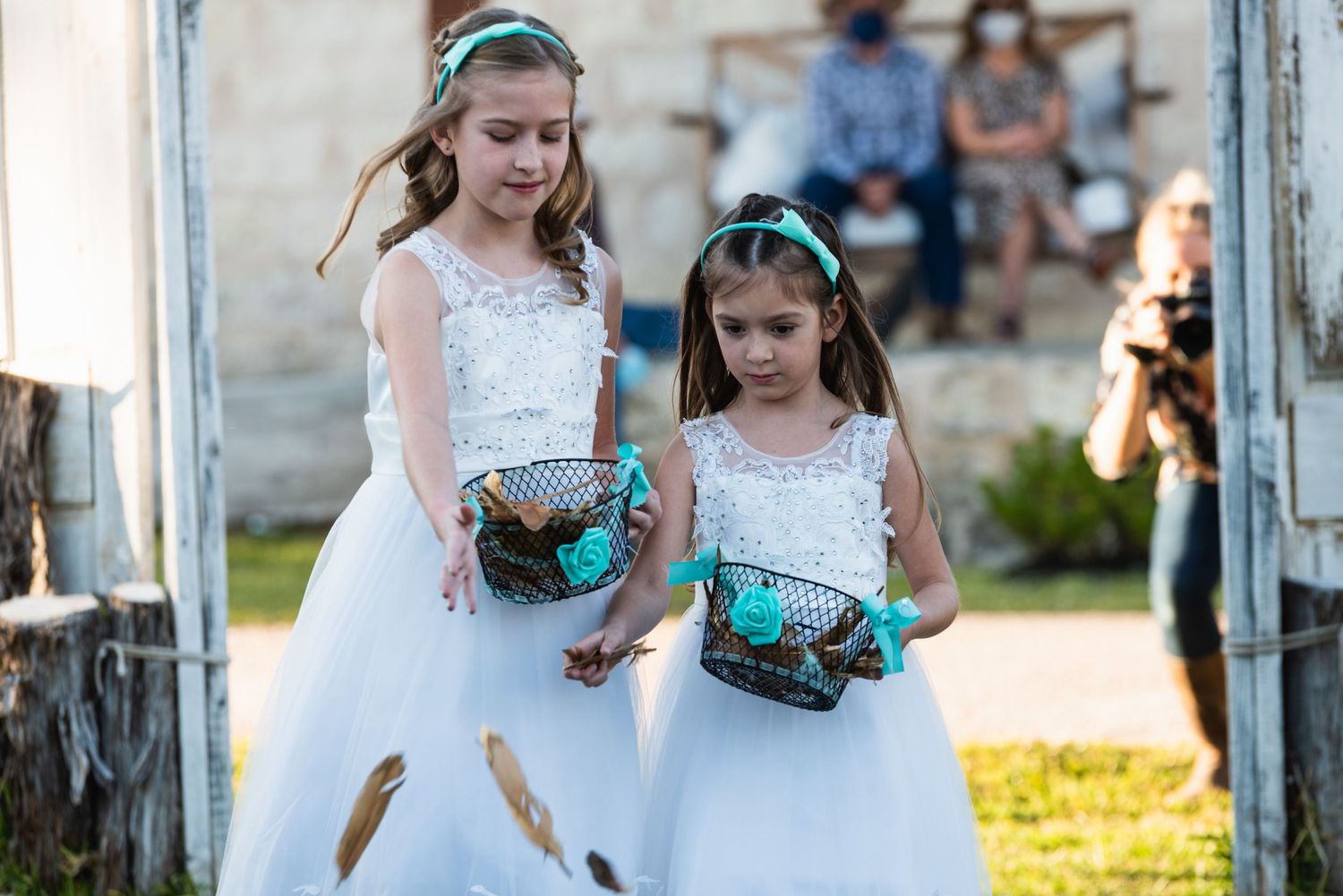 Two flower girls in white dresses carry matching turquoise baskets down the aisle.
