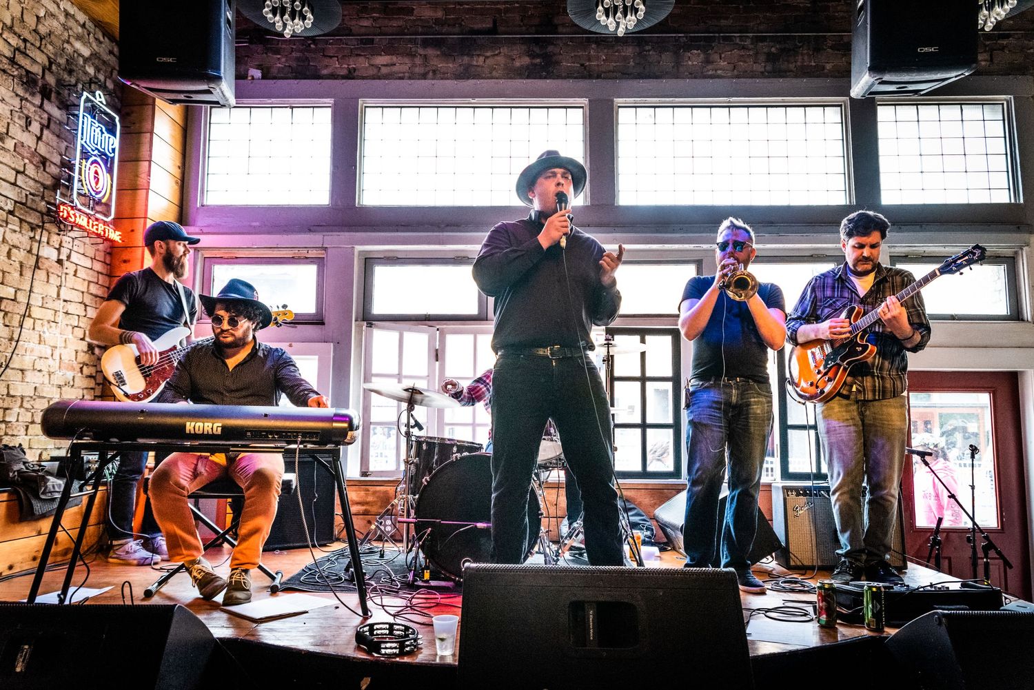 Band performing on stage with various instruments including keyboard, brass, and guitar in color photo.