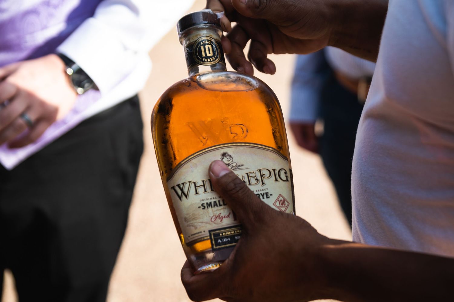 Close-up of hands holding a bottle of WhistlePig whiskey during wedding celebrations.