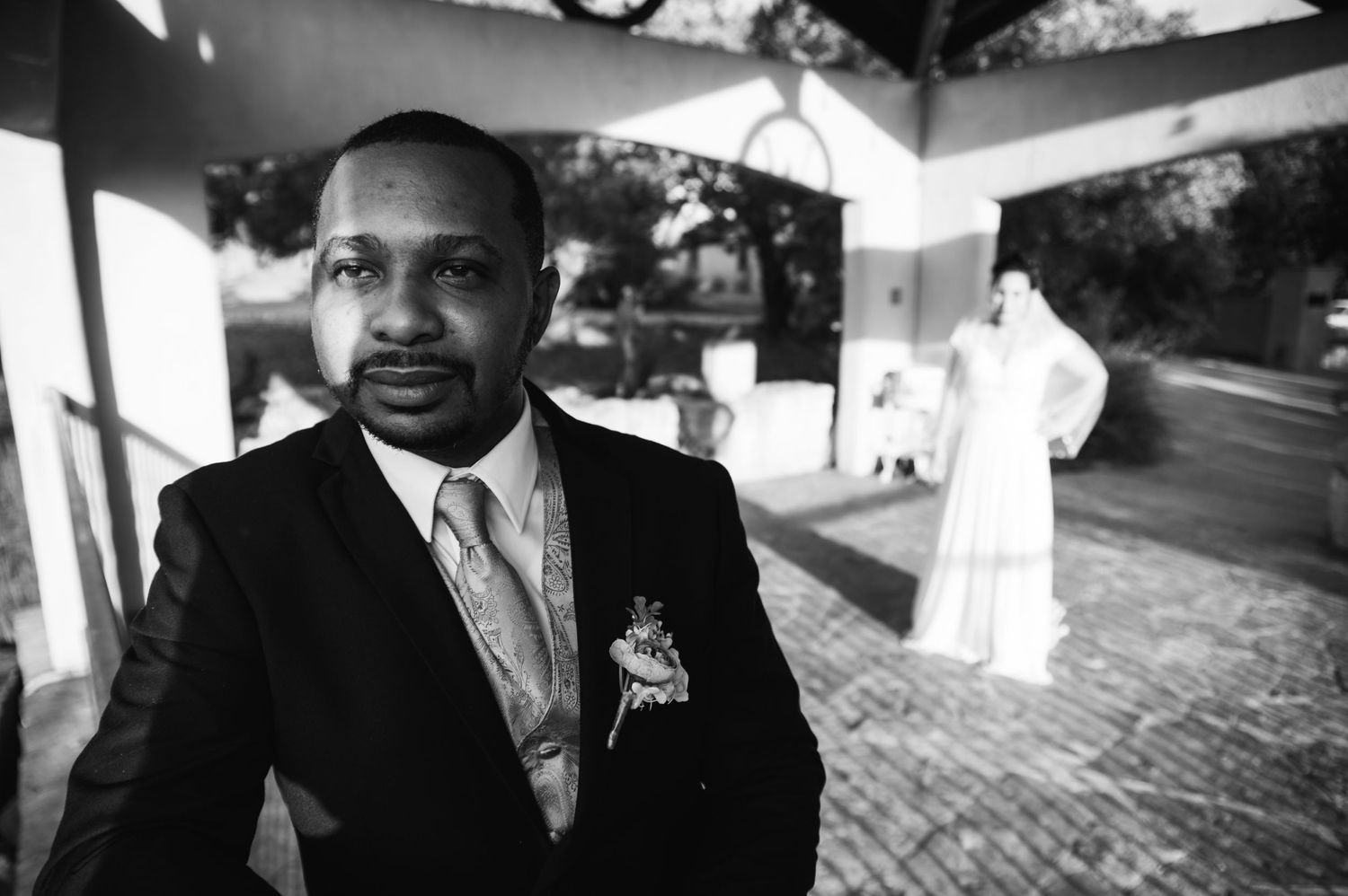 Person in formal suit stands in outdoor wedding venue setting.