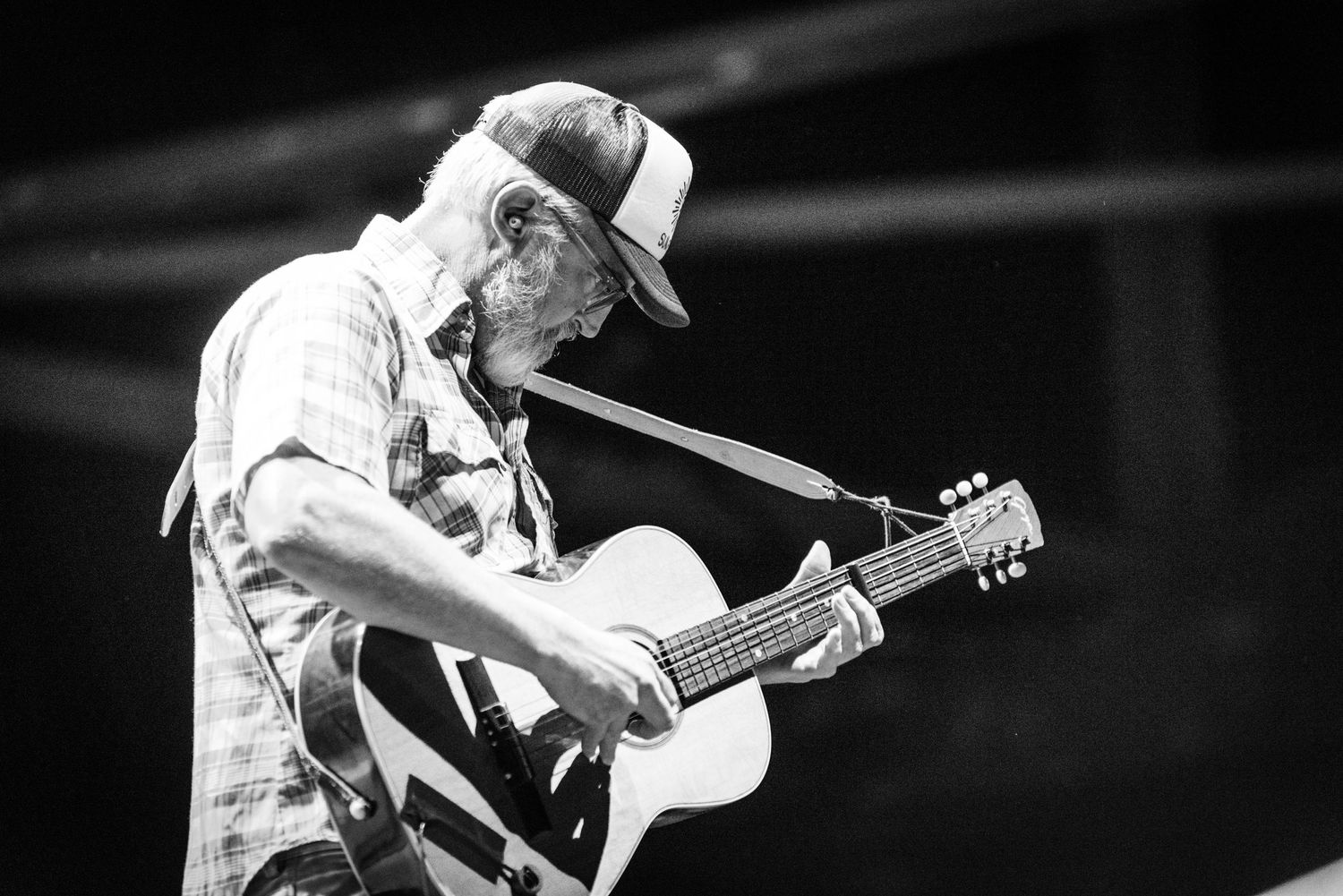 Black and white photo of musician playing acoustic guitar during live performance.