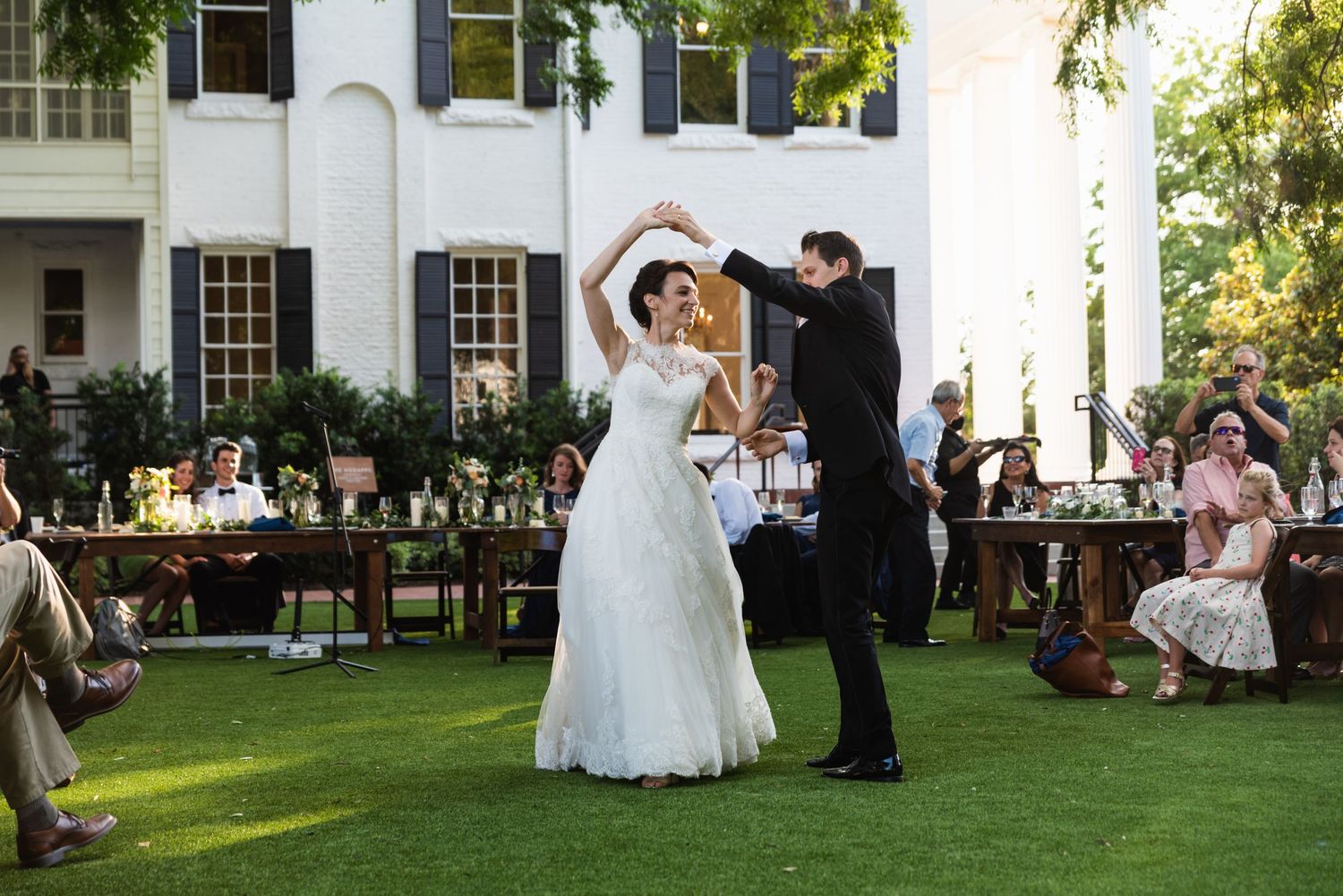 Couple shares their first dance on a manicured lawn during an outdoor wedding reception.