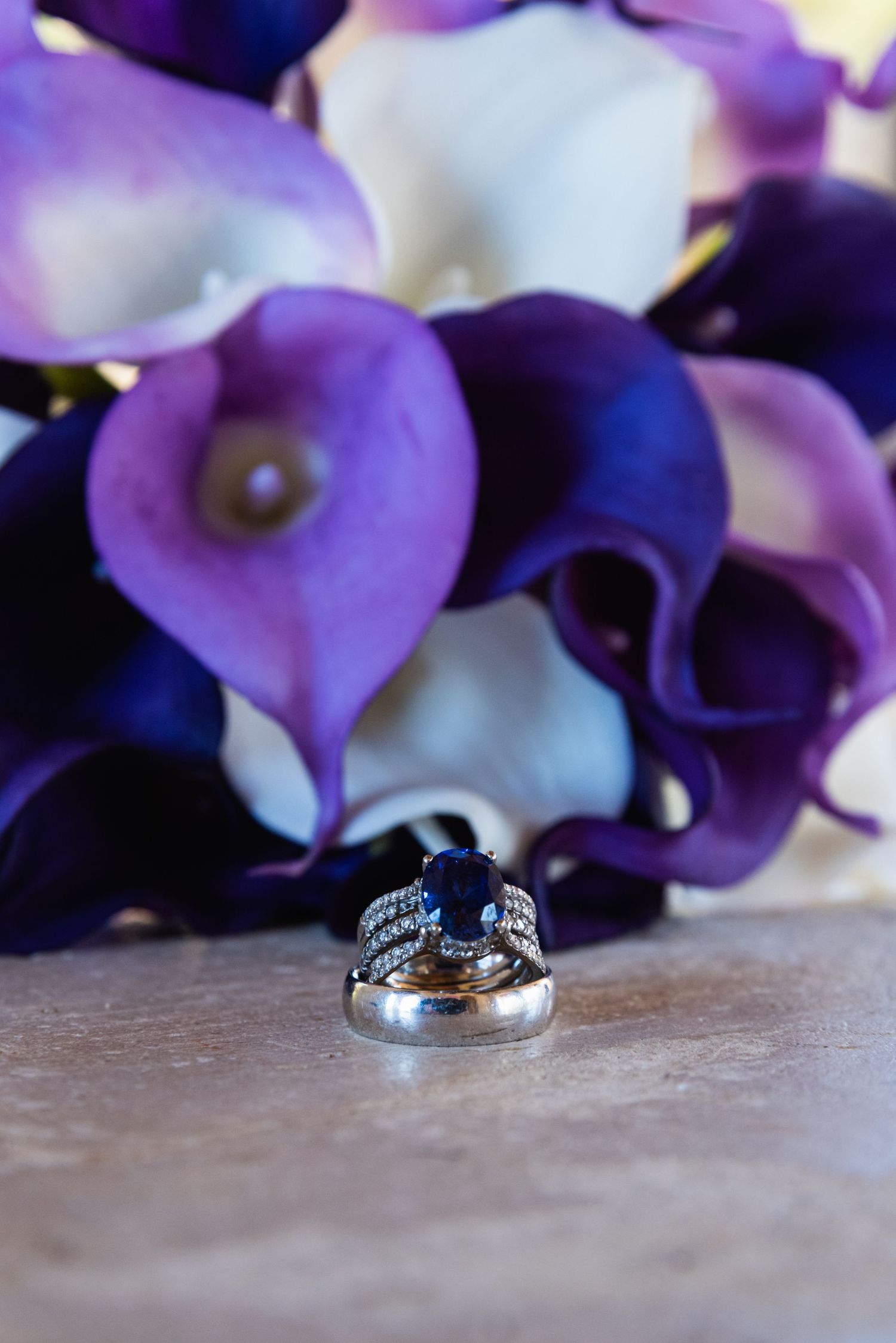 Wedding rings photographed with purple and white calla lilies in the background.