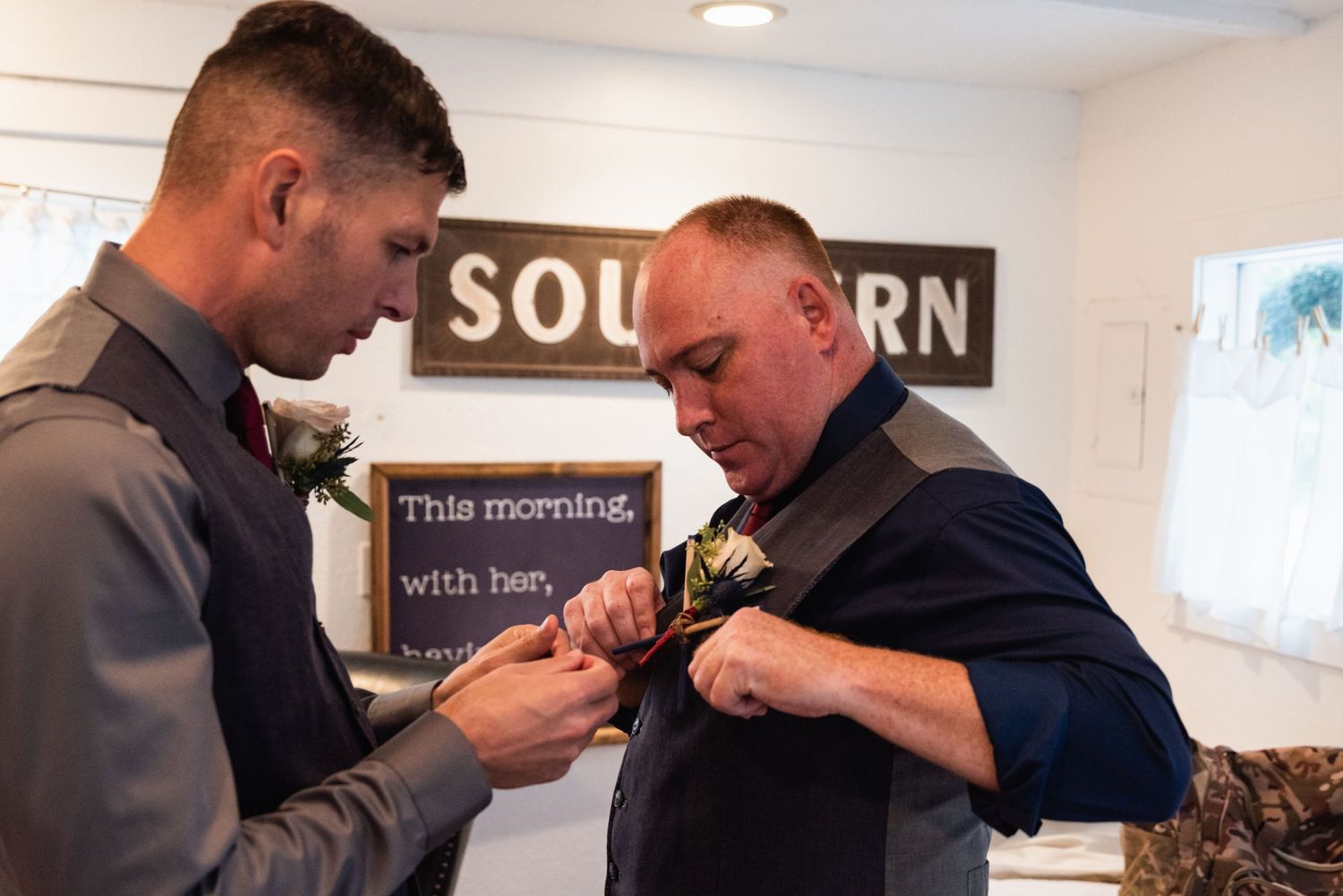 Two men help each other pin boutonnieres on their formal attire.