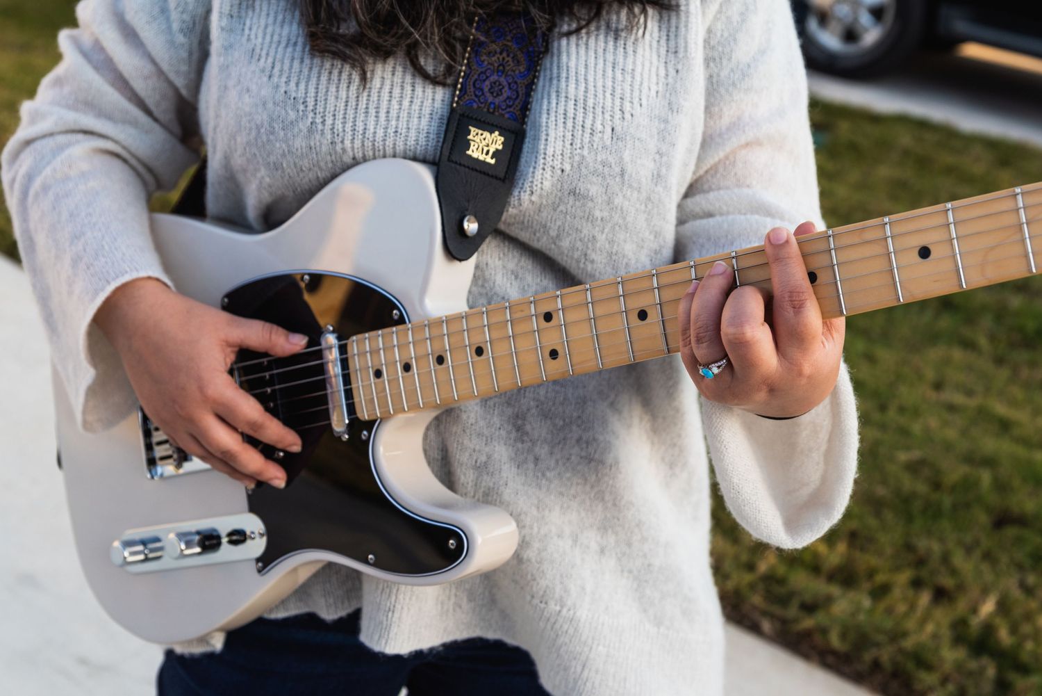 Detail shot of hands playing a white Telecaster guitar with black pickguard.